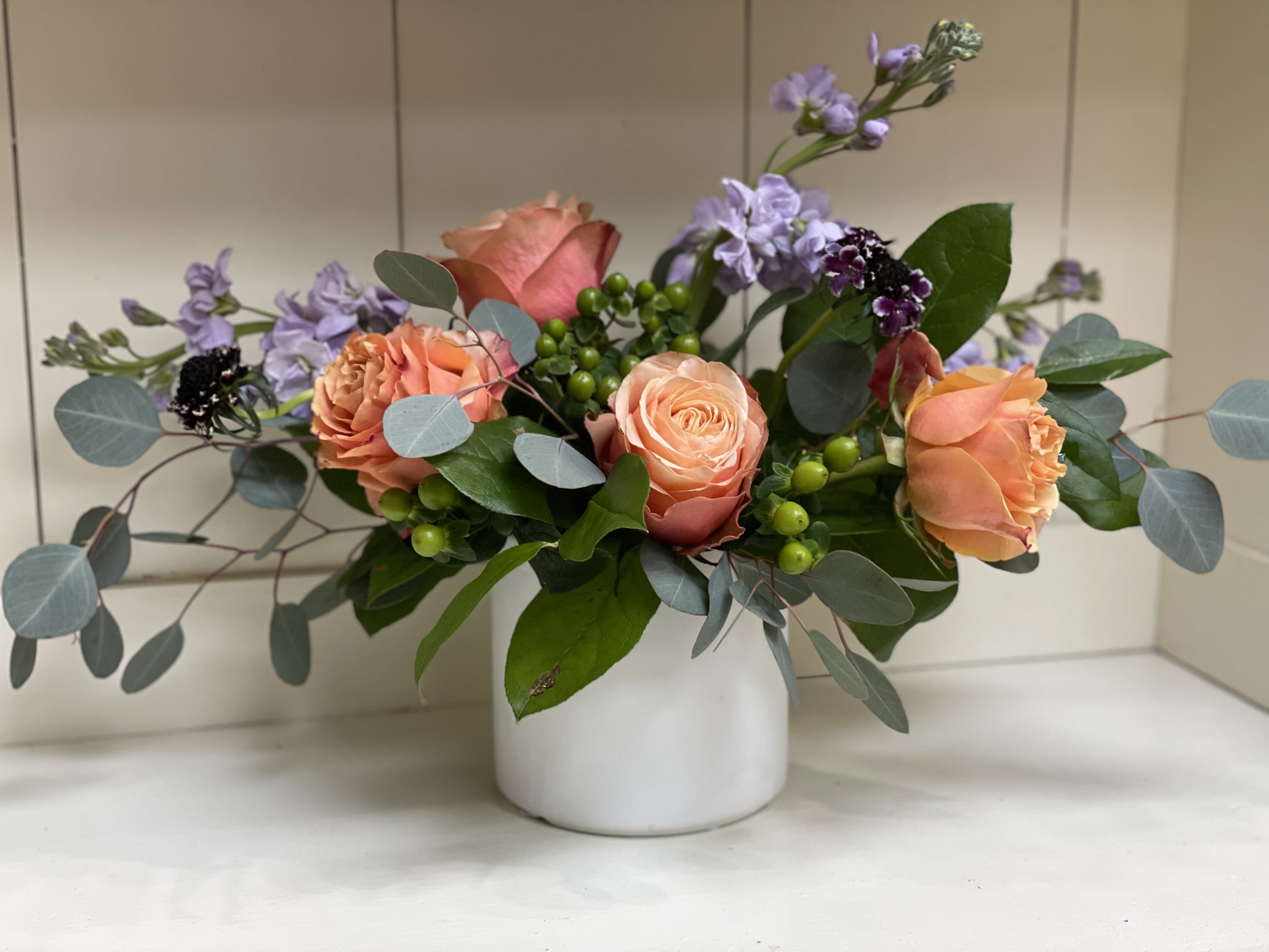 Peach roses and lavender flowers in a white vase