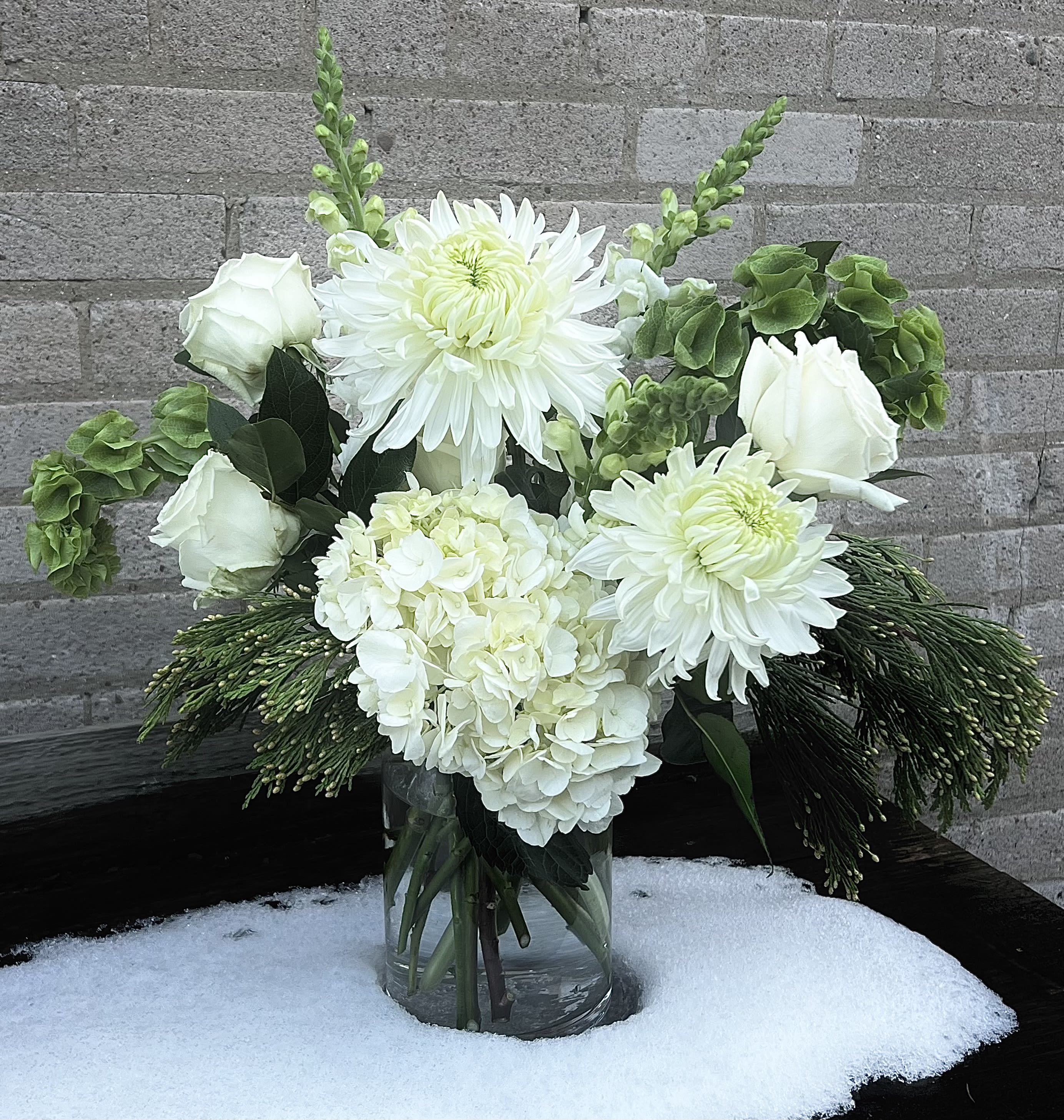 White floral arrangement in a clear glass vase with green accents