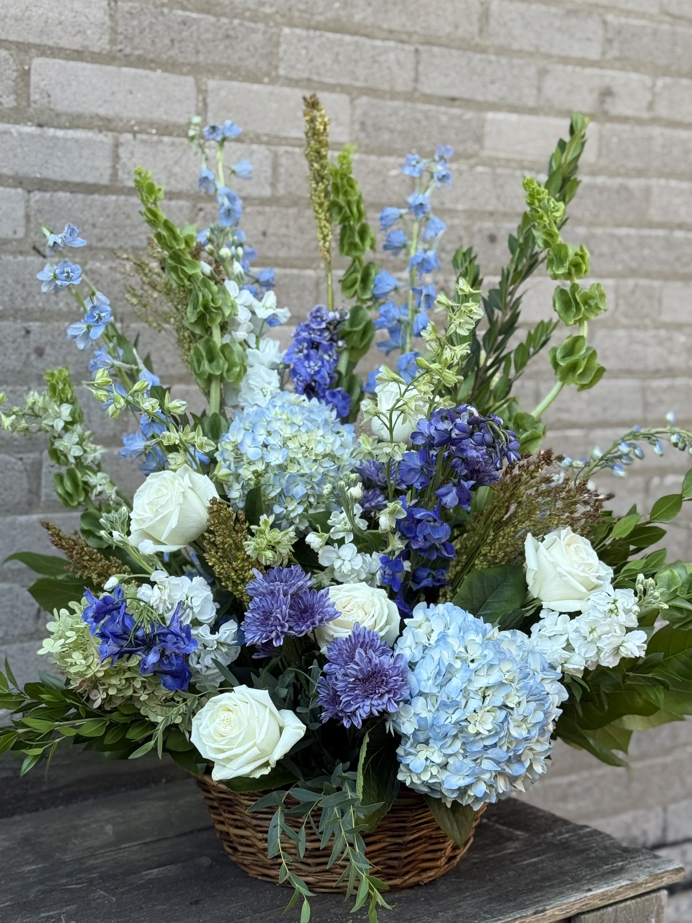 Basket arrangement of blue and white flowers with roses and hydrangeas