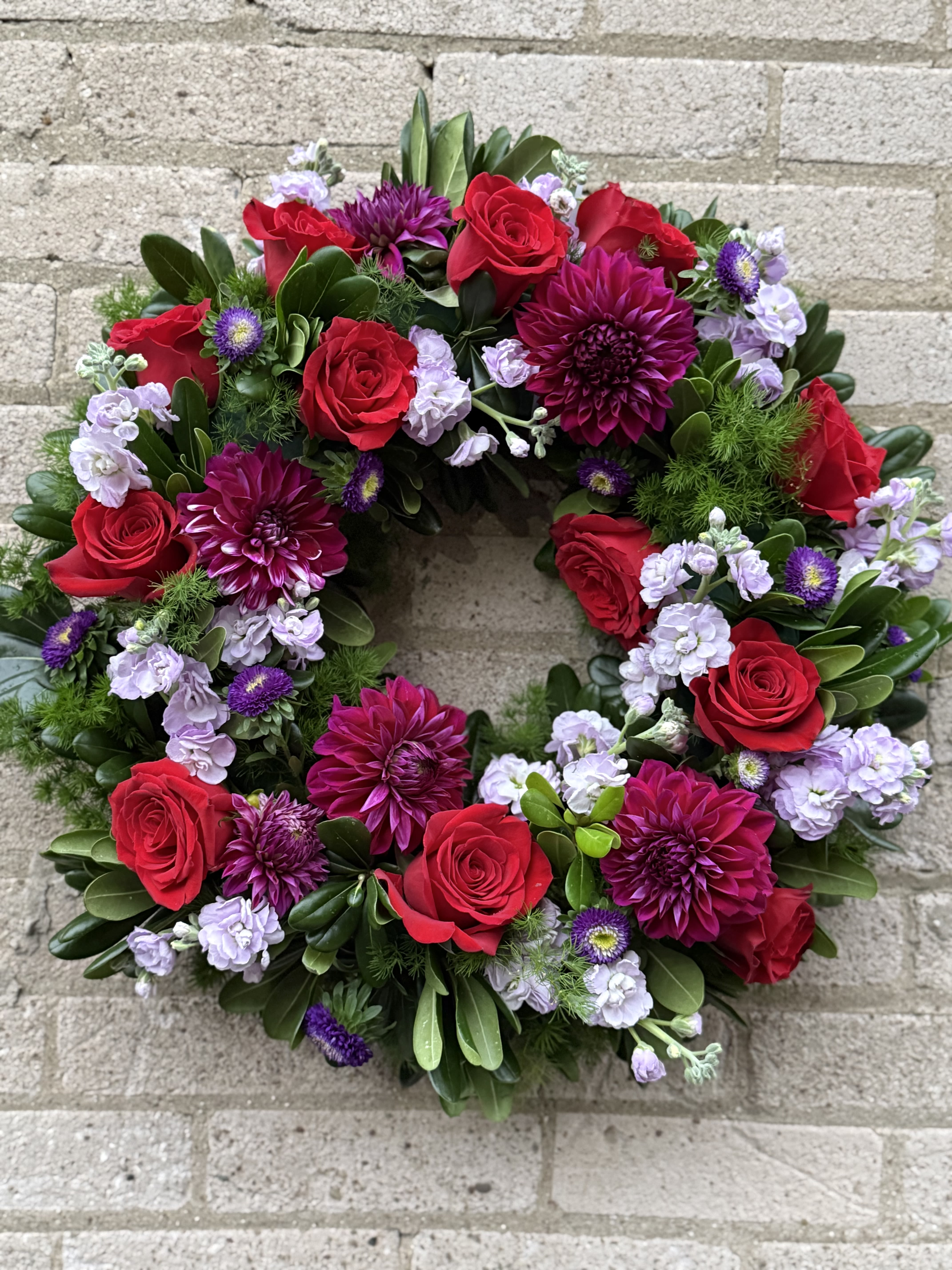 Circular wreath of red roses, purple dahlias, and lavender blooms