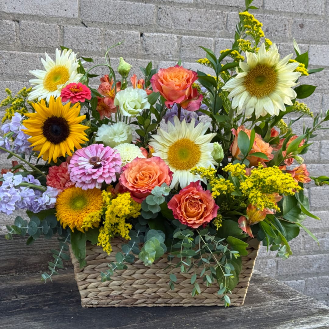 Mixed bouquet in a woven basket with sunflowers, roses, and pastel blooms