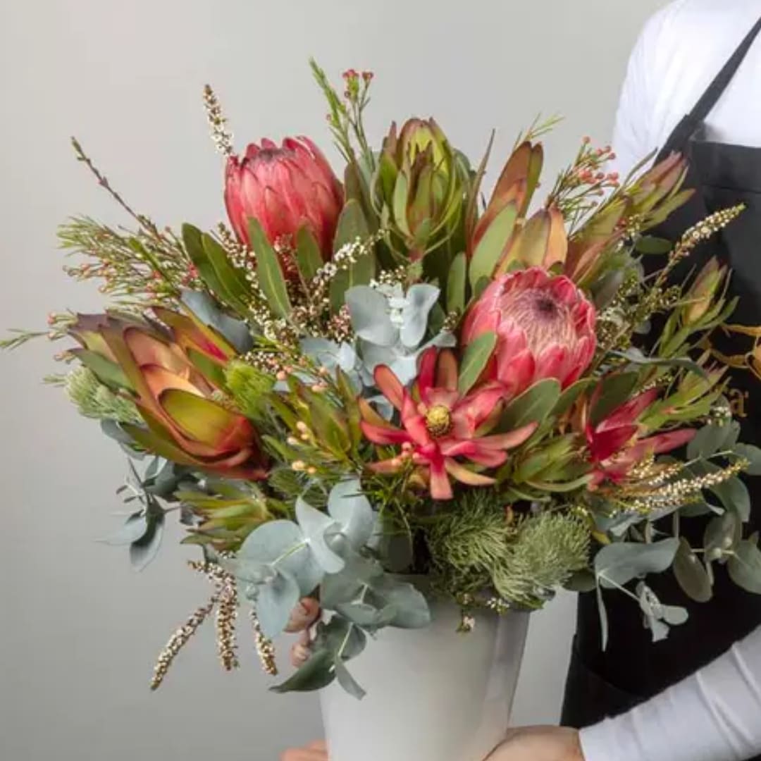 Protea bouquet in a white vase with eucalyptus and pink blooms