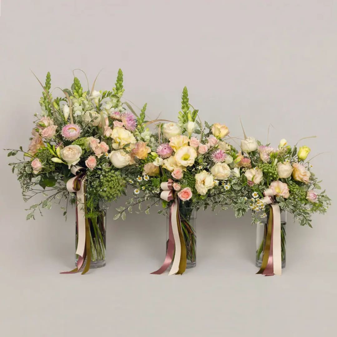 Three pastel floral arrangements in glass vases with ribbon streamers