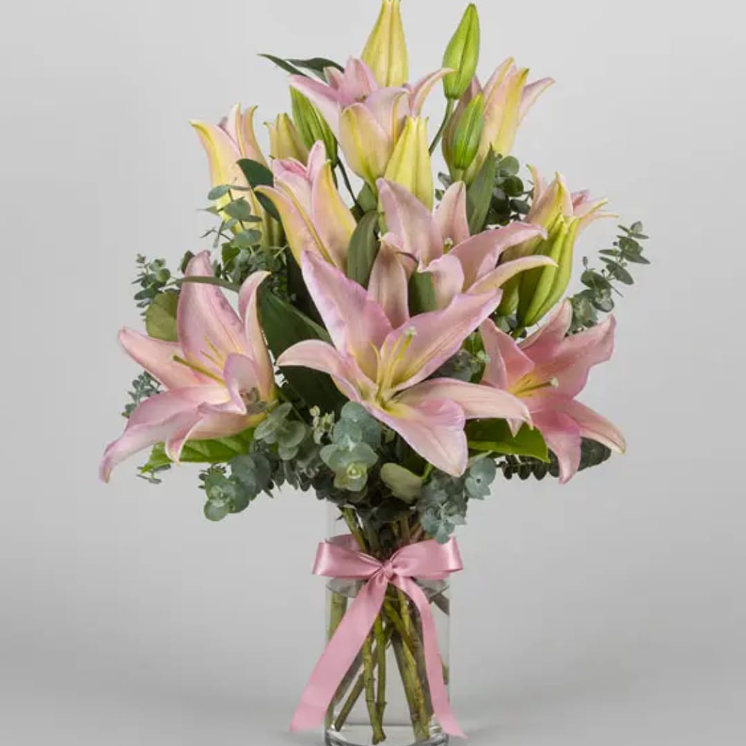 Pink and yellow lilies arranged in a clear glass vase with a pink ribbon