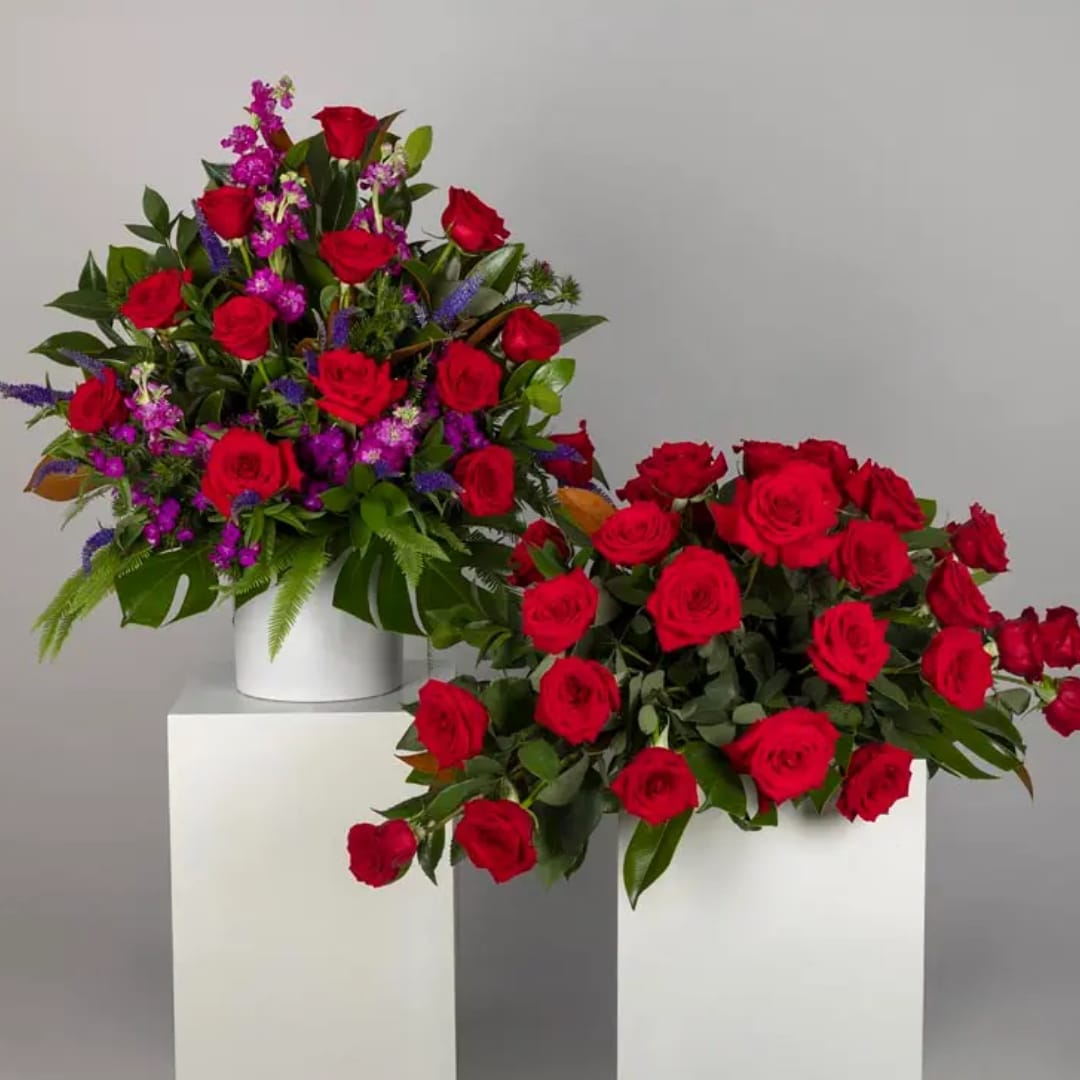 Two red rose arrangements on white pedestals against a gray background