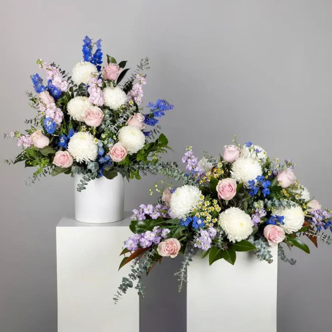 Two pastel floral arrangements in white vases on pedestals