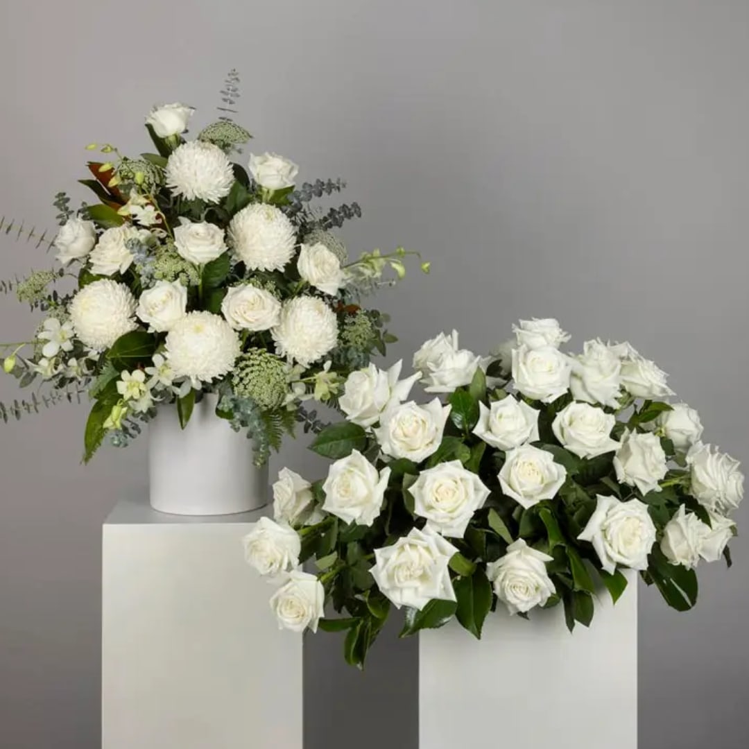 Two white floral arrangements in white containers on pedestals