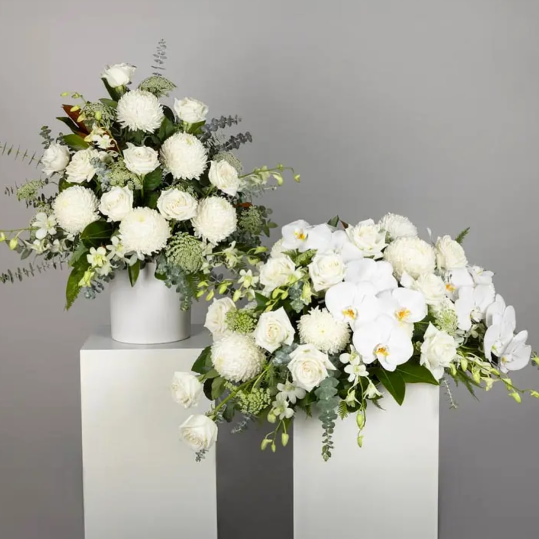 Two white floral arrangements in white pedestal vases