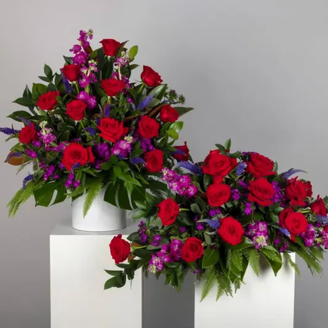 Two red rose arrangements with purple accents in white containers