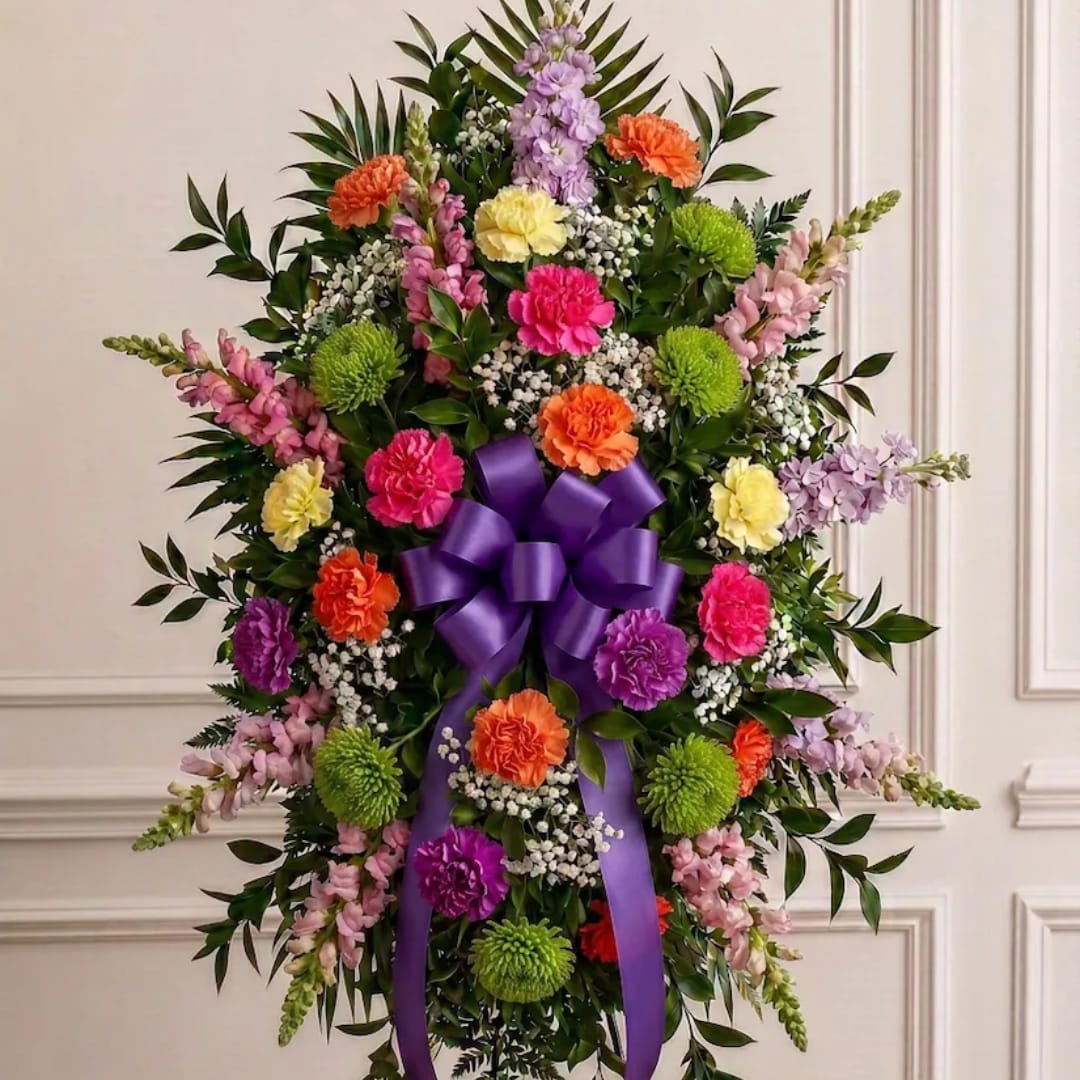 Standing floral spray with a purple ribbon bow and mixed blooms