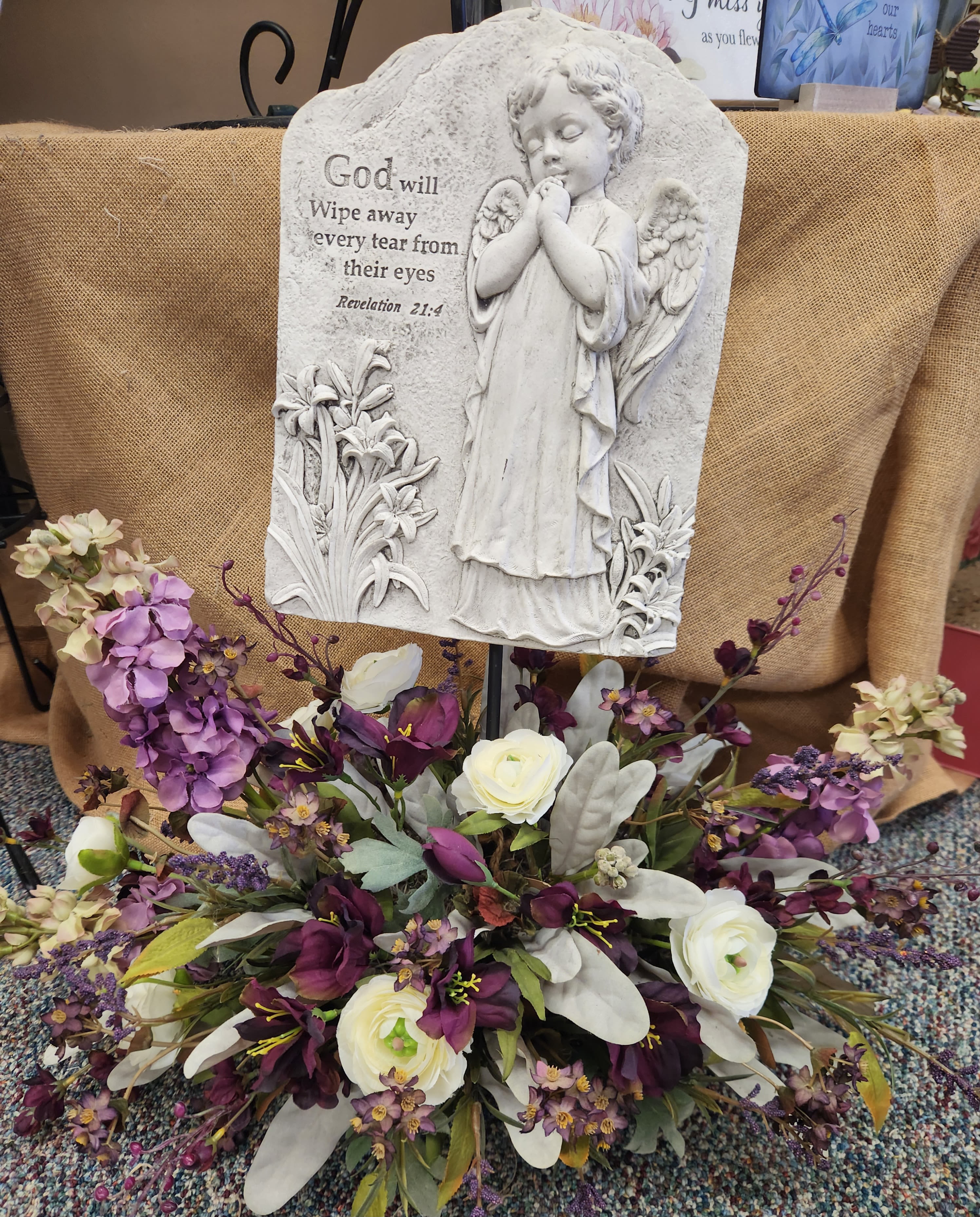 Memorial plaque with angel relief above a purple and white floral arrangement