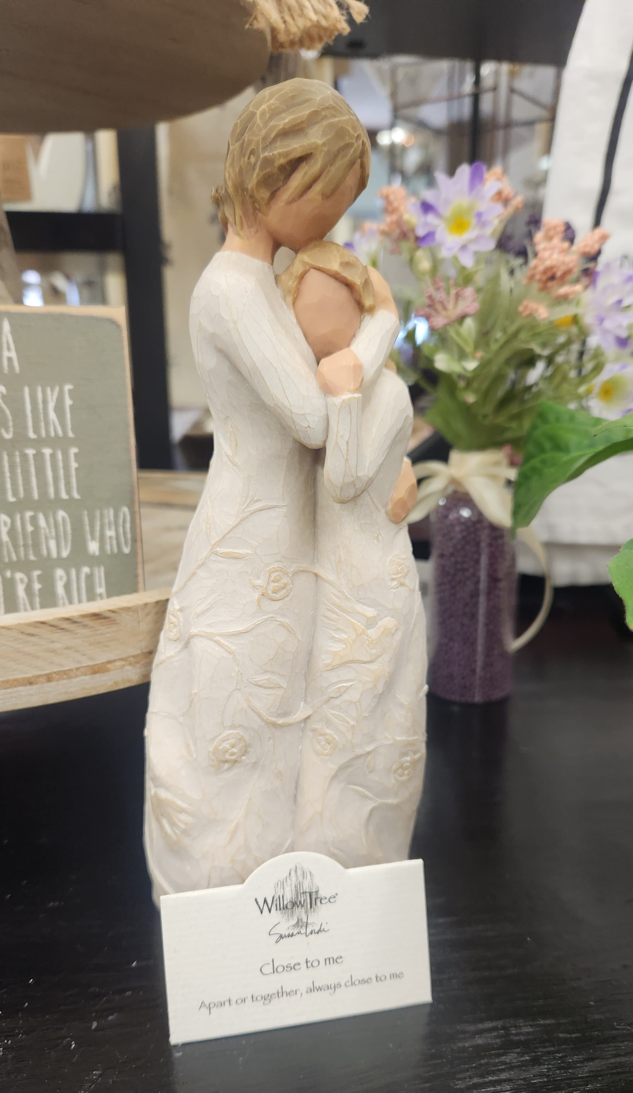 Decorative figurine of two people embracing, with a small flower arrangement behind it