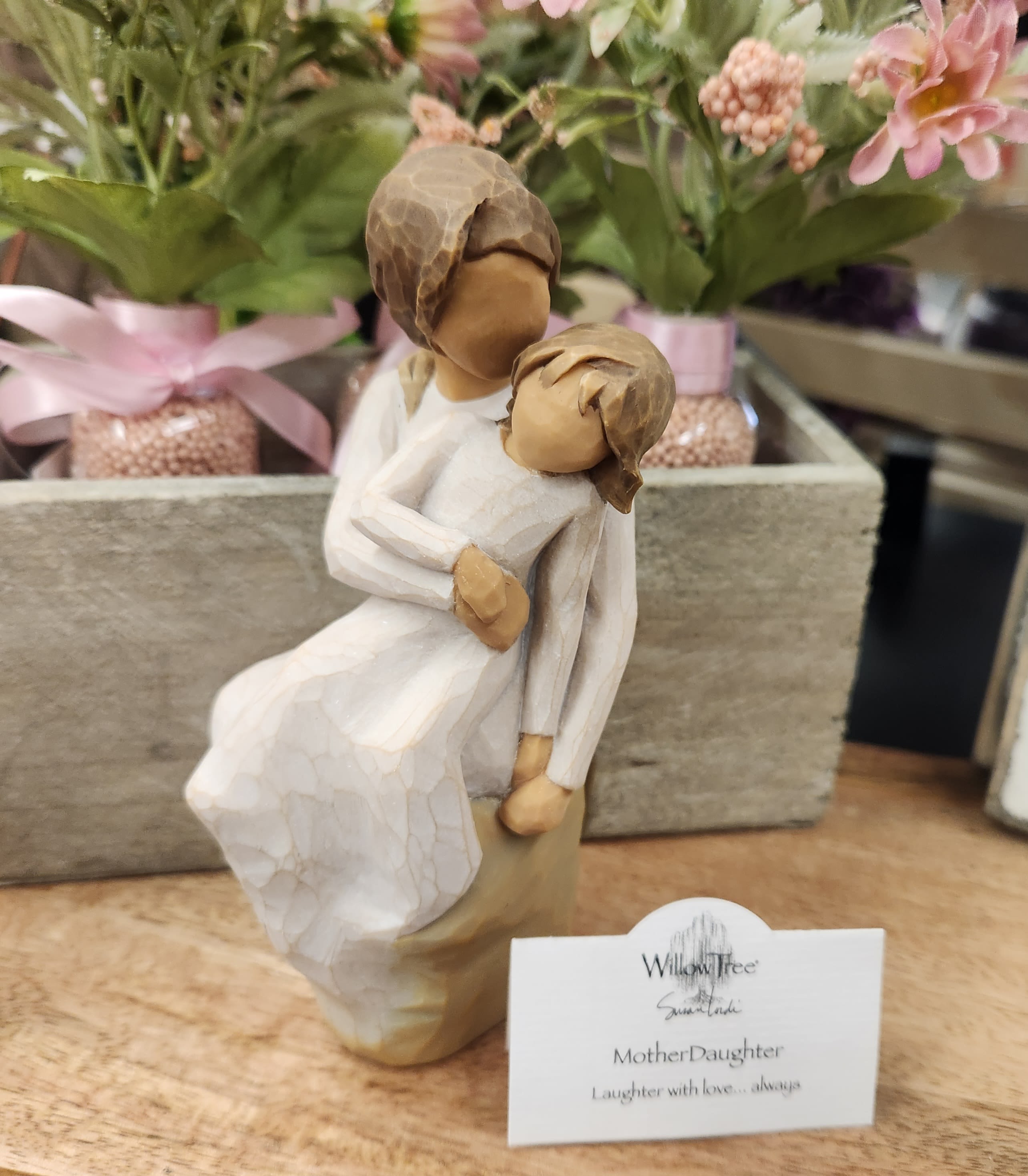 Wooden mother and daughter figurine in front of pink potted flowers