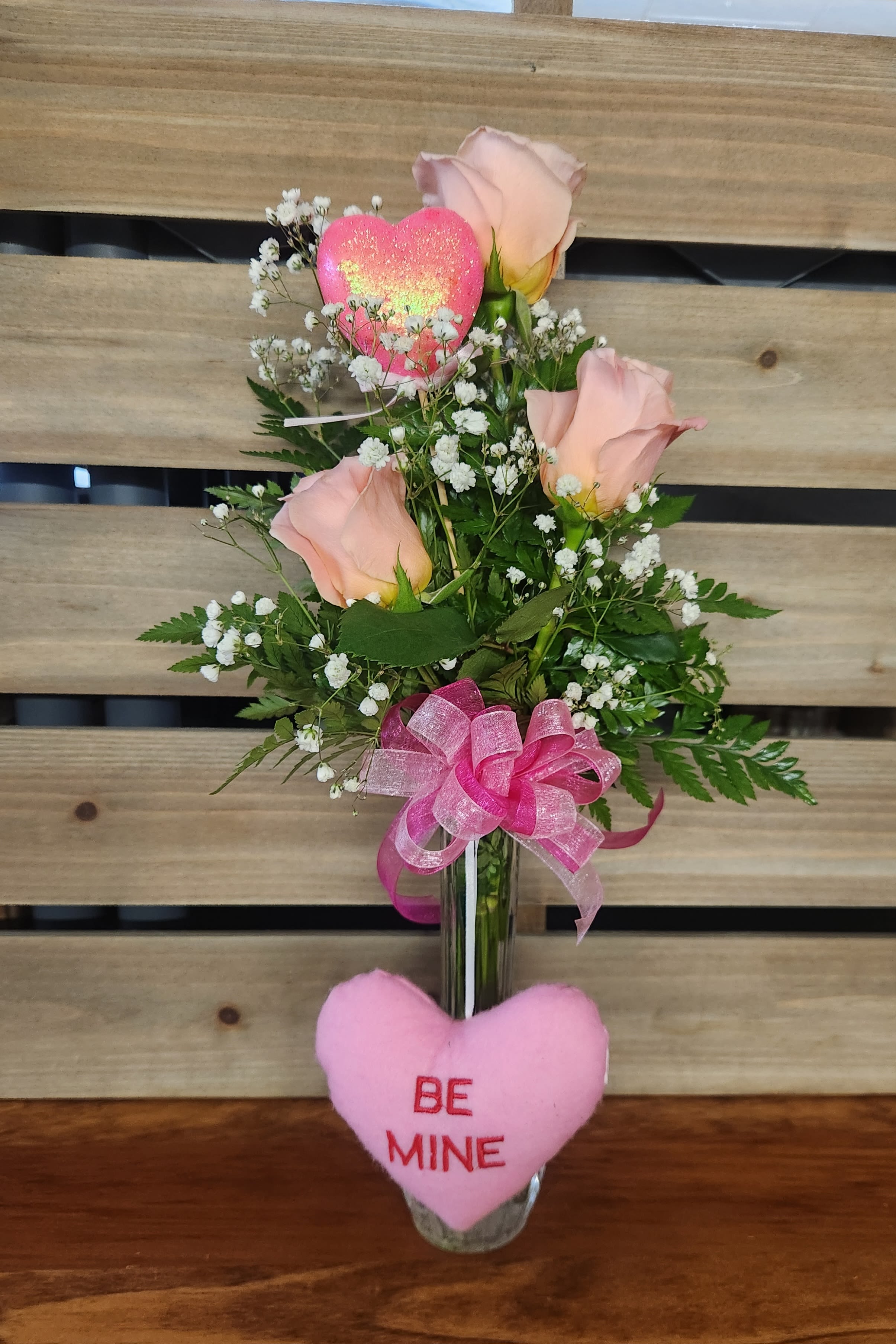 Pink roses in a glass vase with a heart topper and ribbon
