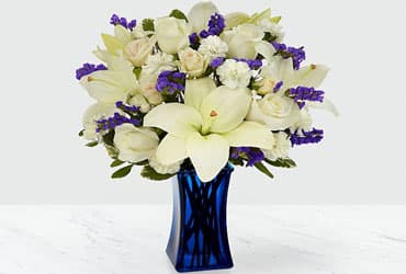 White lilies and roses with purple accents in a blue vase