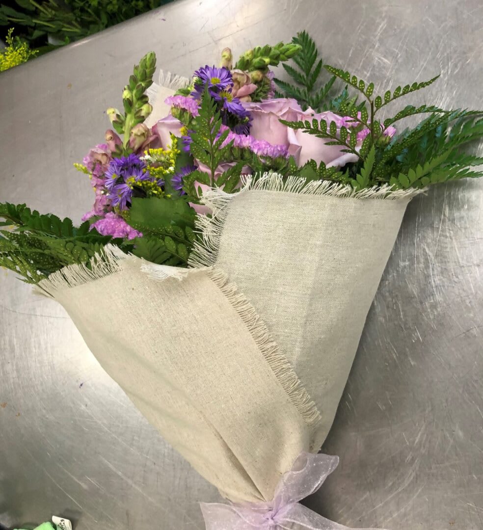 Bouquet of pink roses and purple flowers wrapped in beige fabric