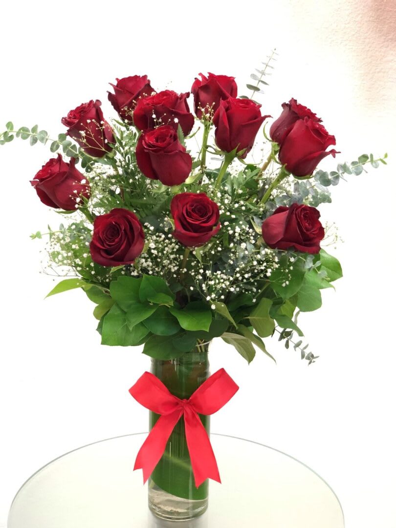 Red roses arranged in a glass vase with a red ribbon