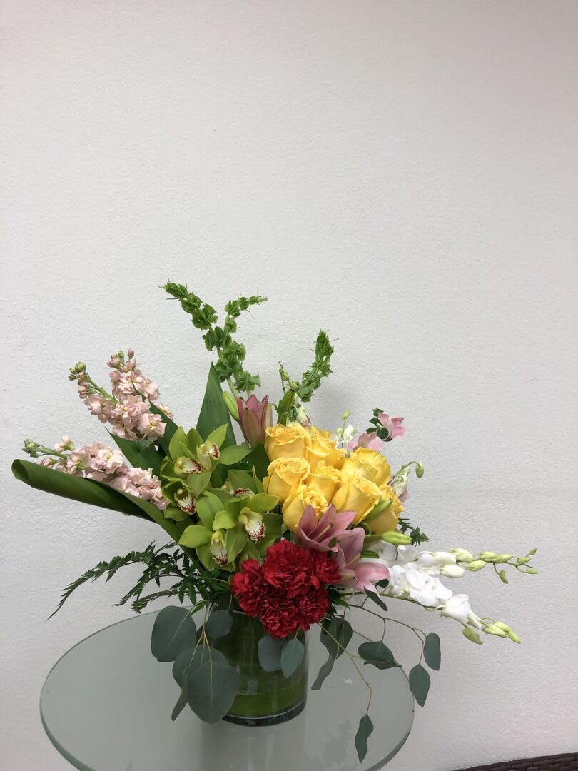 Mixed bouquet in a glass vase with yellow roses, pink blooms, and white orchids