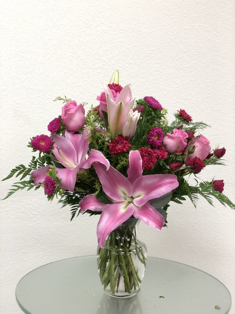 Pink lilies and roses arranged in a clear glass vase
