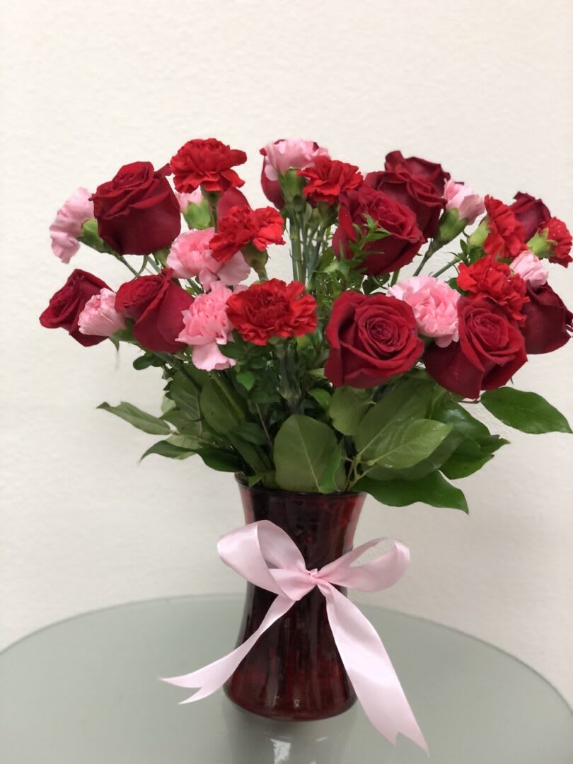Red roses and pink carnations in a burgundy vase with a pink ribbon