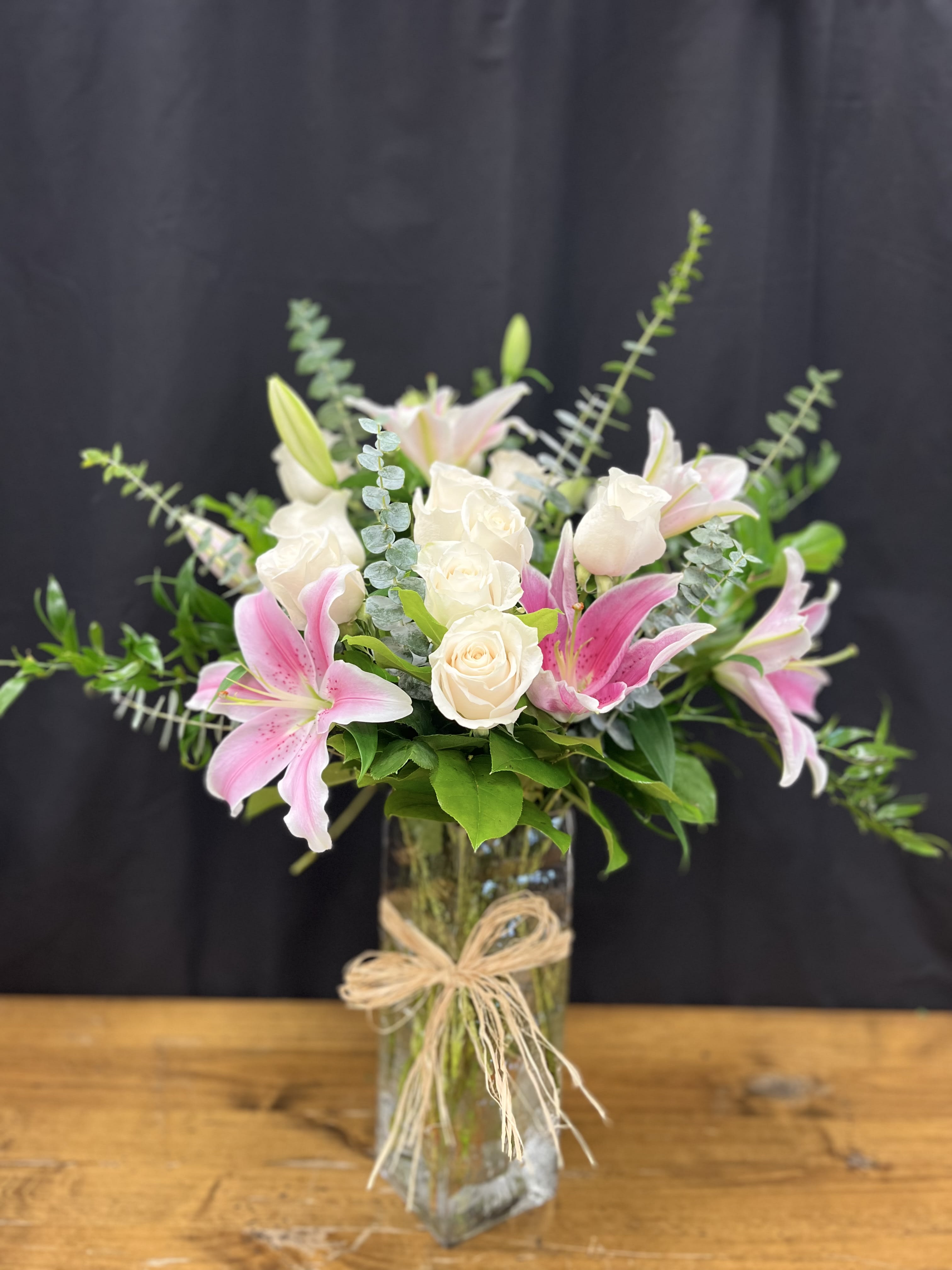 Pink lilies and white roses in a glass vase with a raffia bow