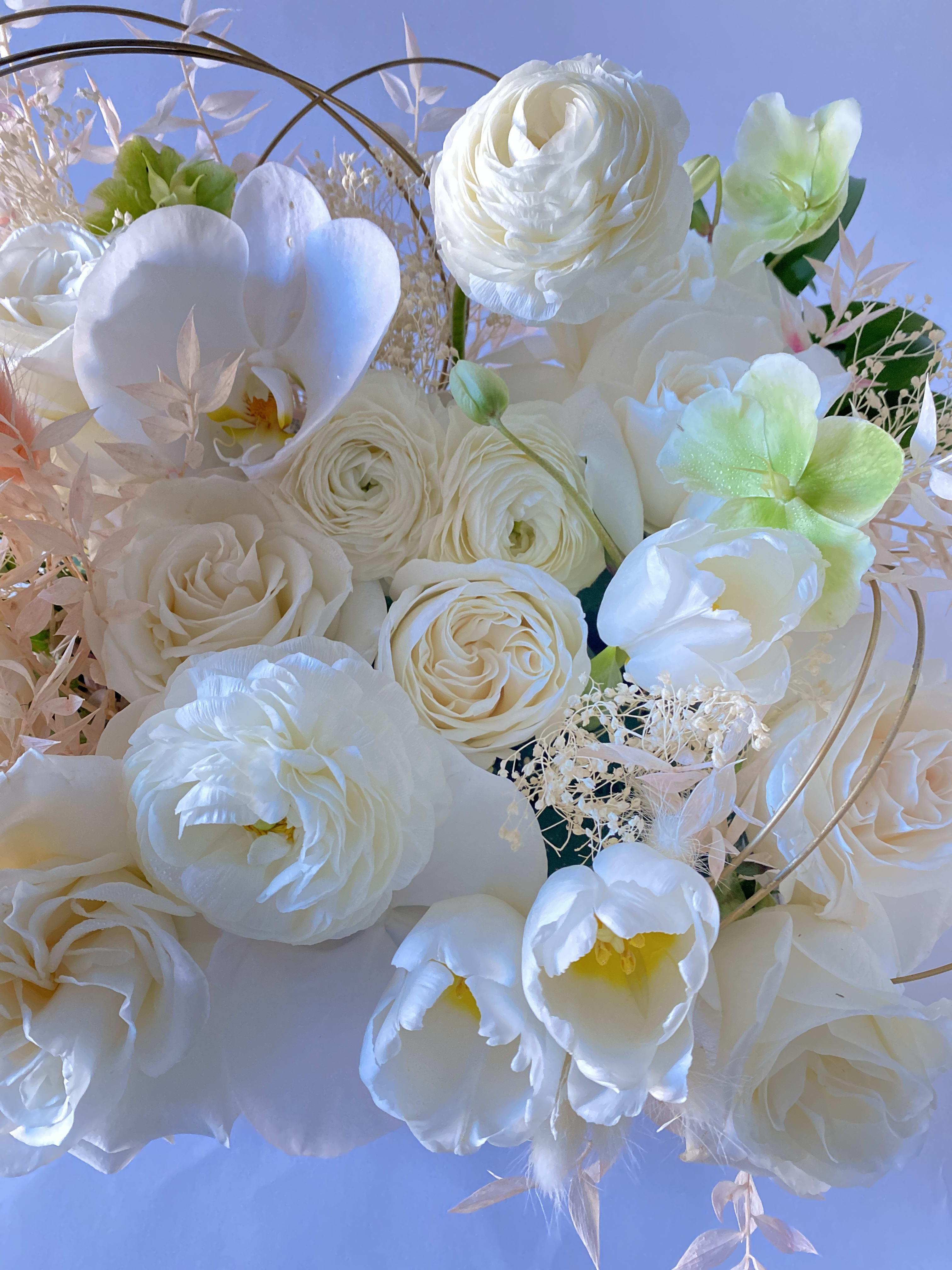 White bouquet with roses, ranunculus, and orchids against a blue background