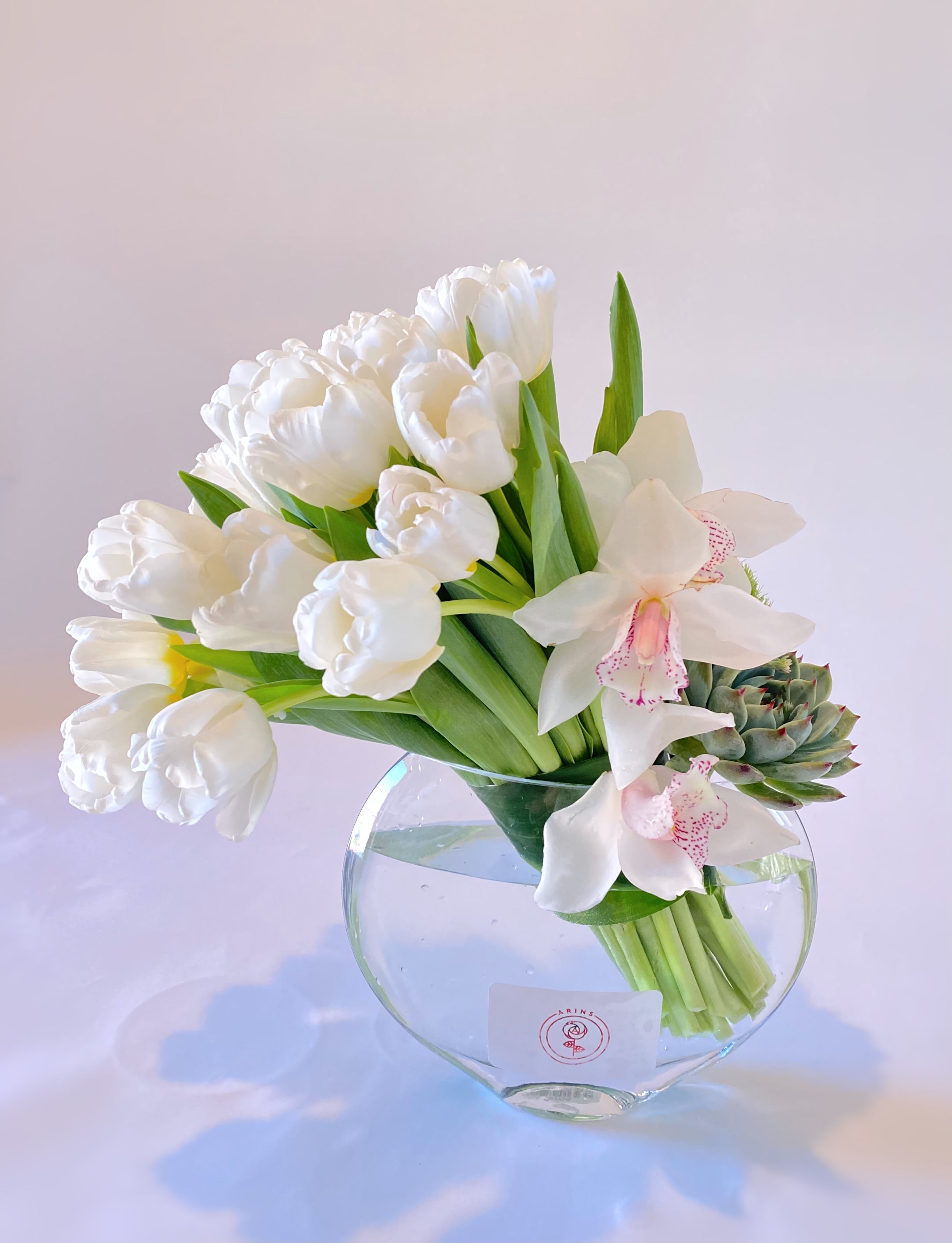 White tulips and orchids arranged in a clear glass vase with a succulent accent