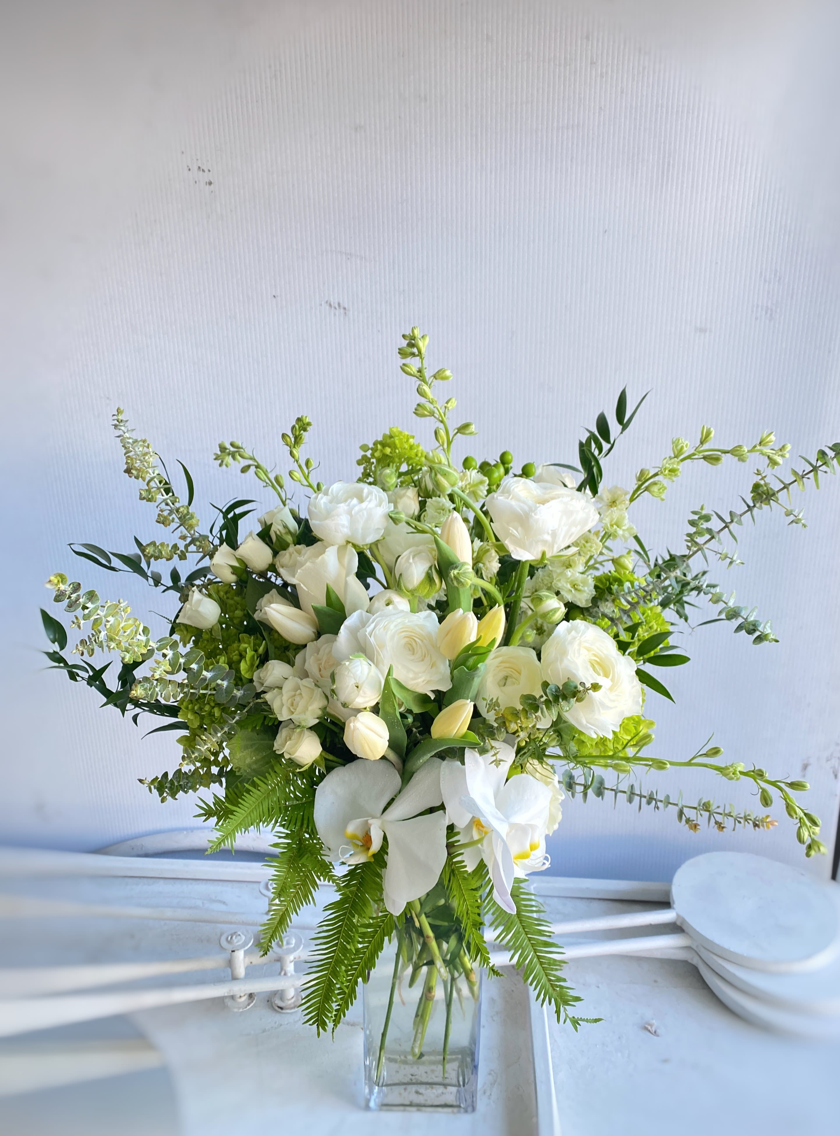 White floral arrangement in a clear glass vase with orchids and roses