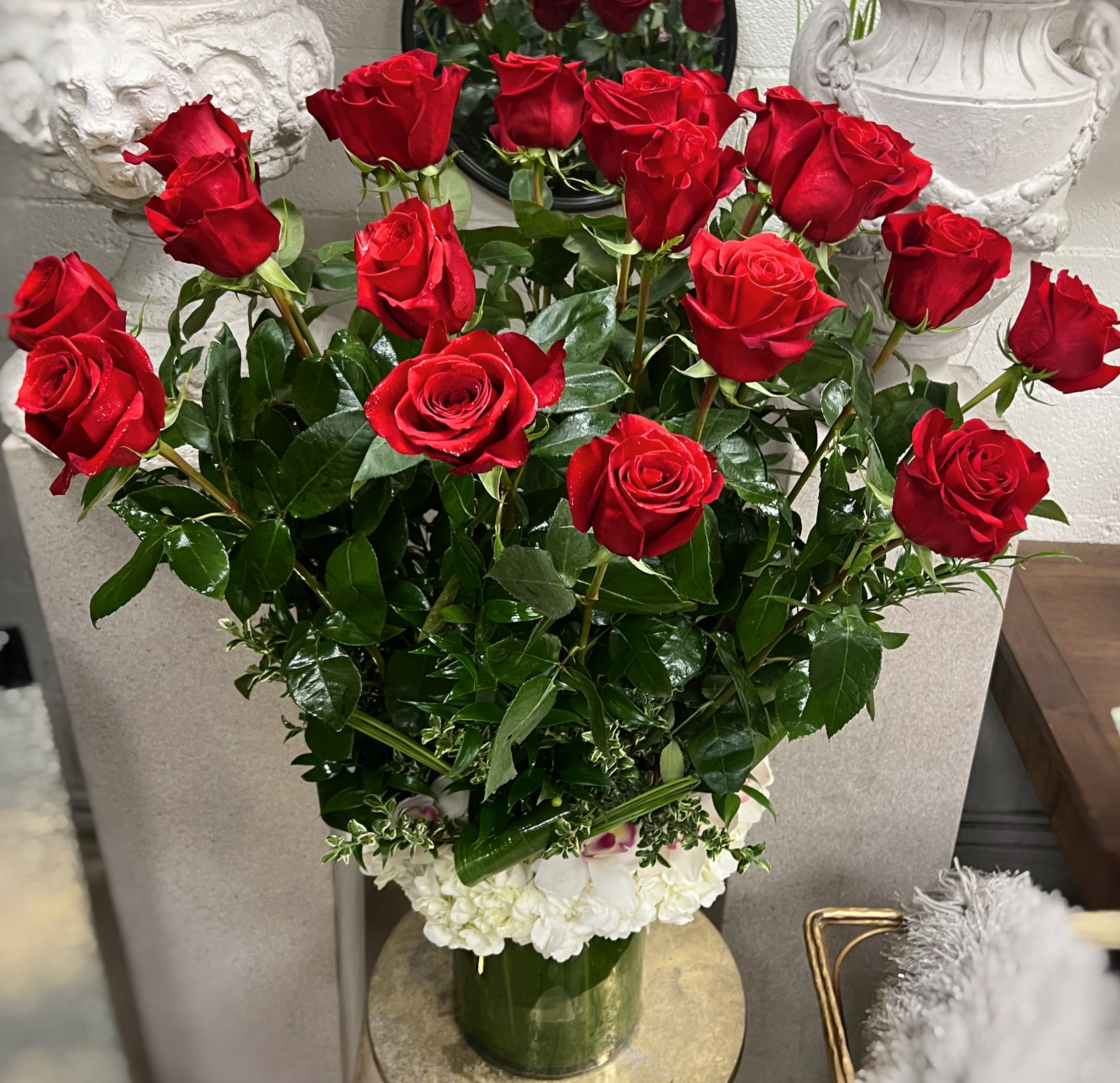 Red roses arranged in a clear vase with white flowers at the base