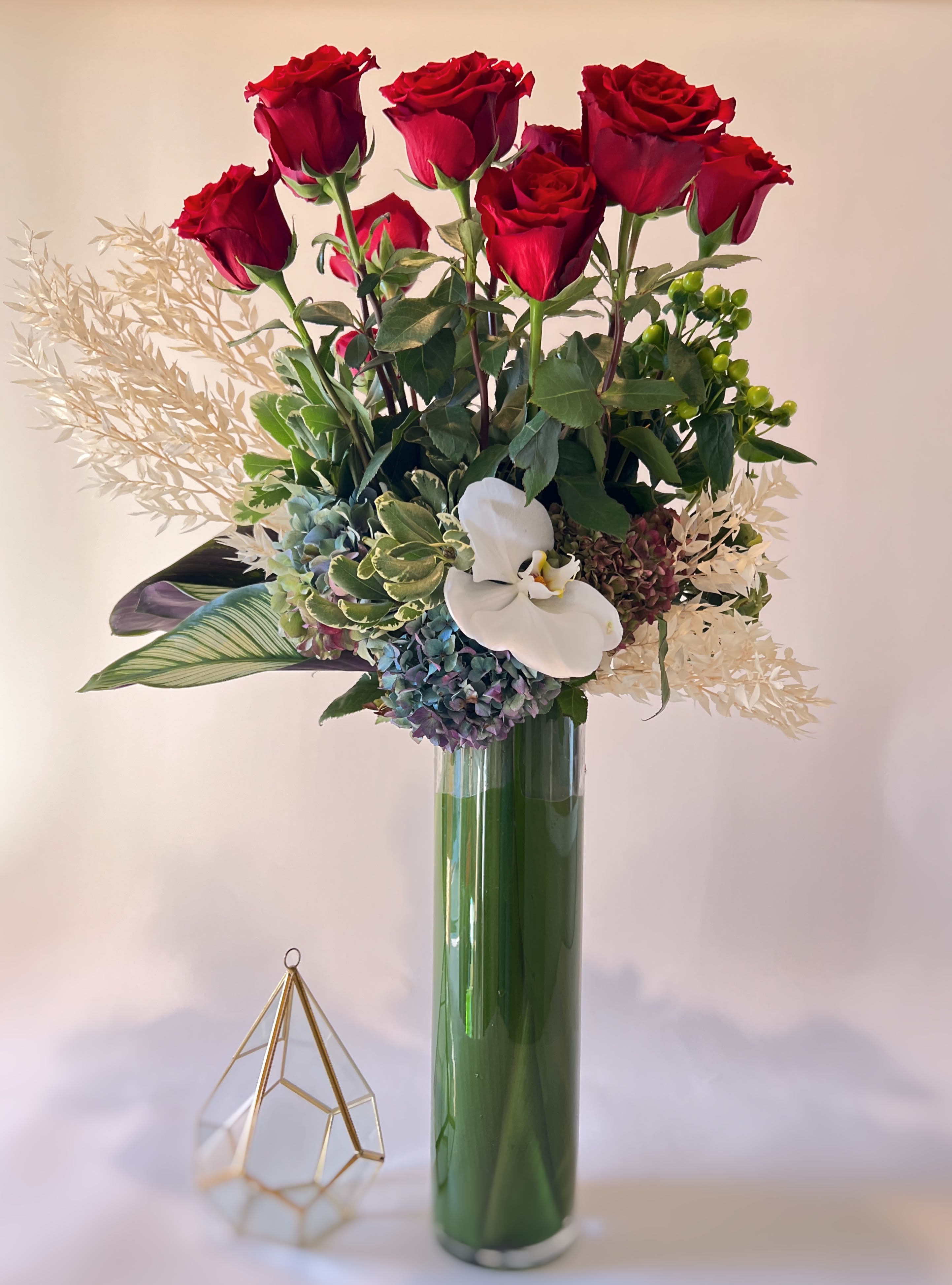Red roses and a white orchid in a tall glass vase