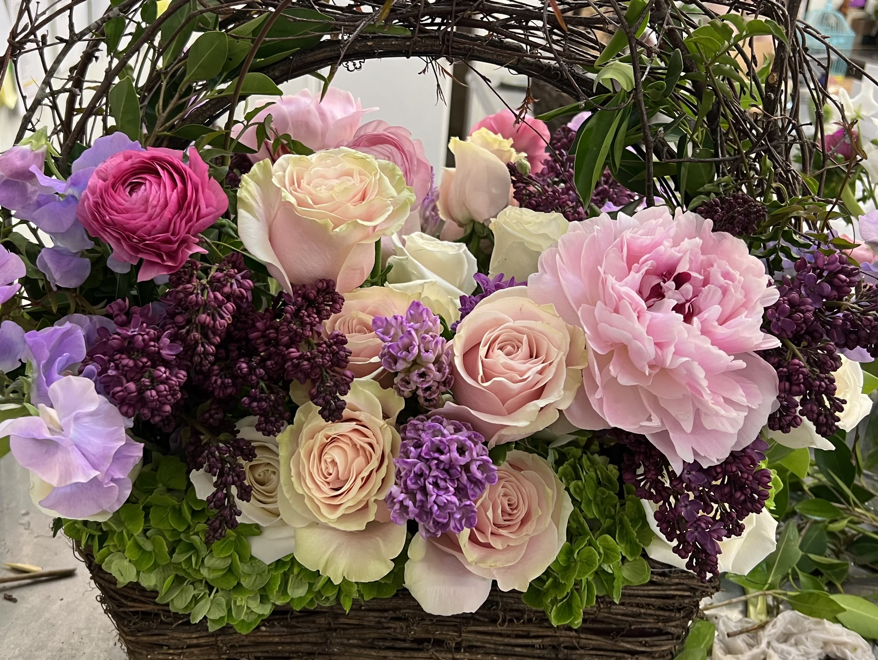 Basket arrangement of pink and lavender roses with peonies and lilac