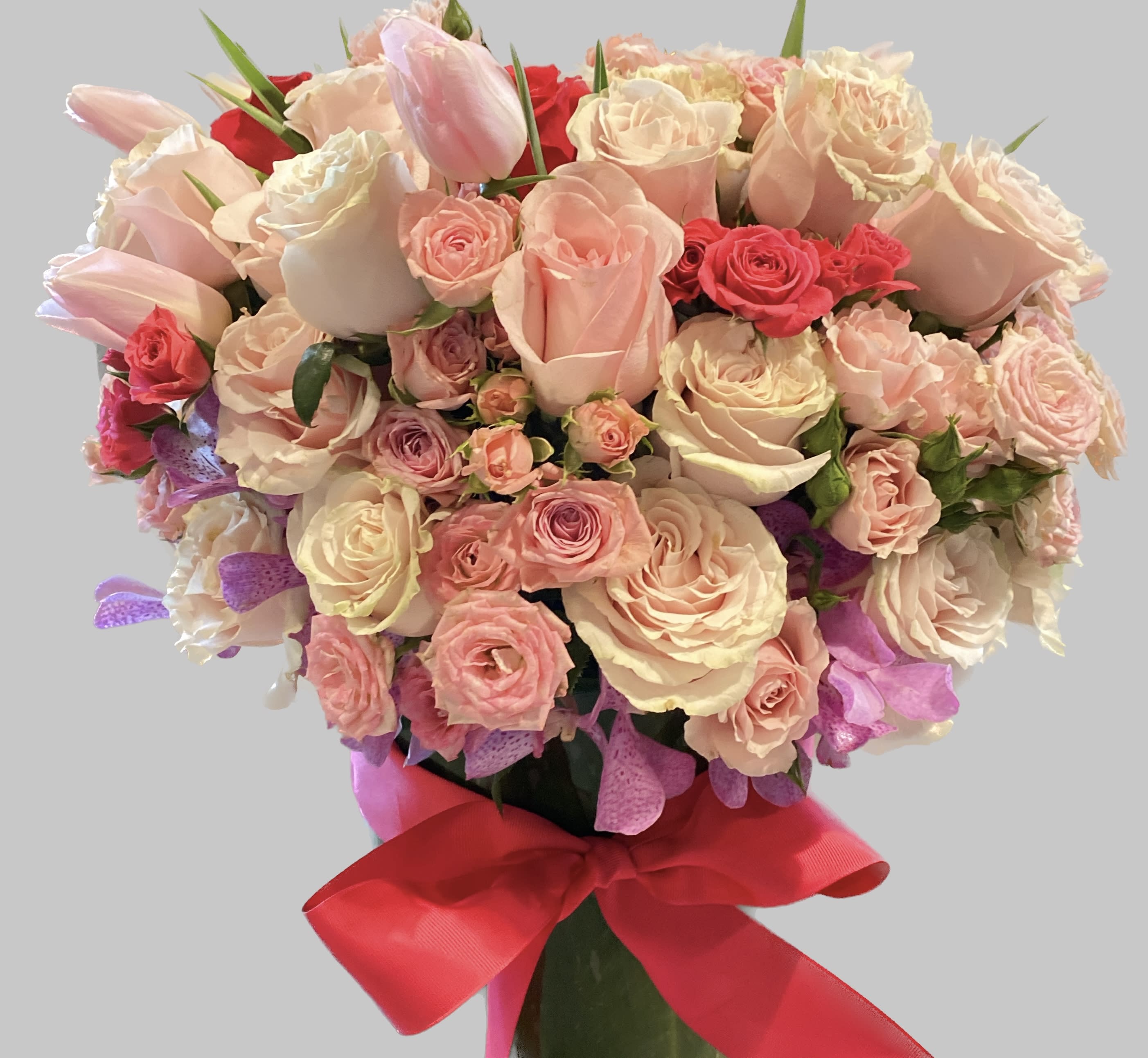 Bouquet of pink and cream roses with tulips tied with a red ribbon
