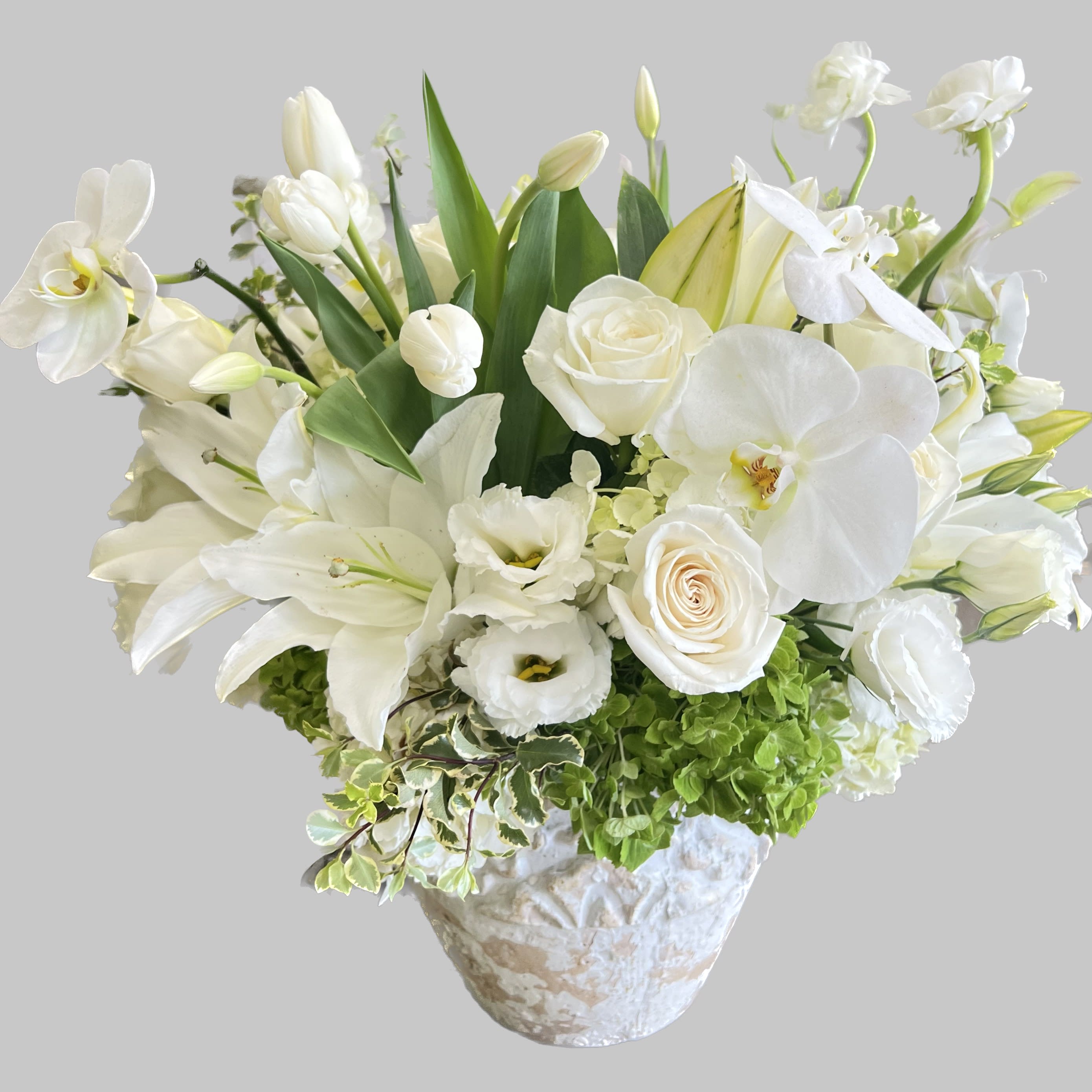 White floral arrangement in a textured vase with lilies, roses, and orchids