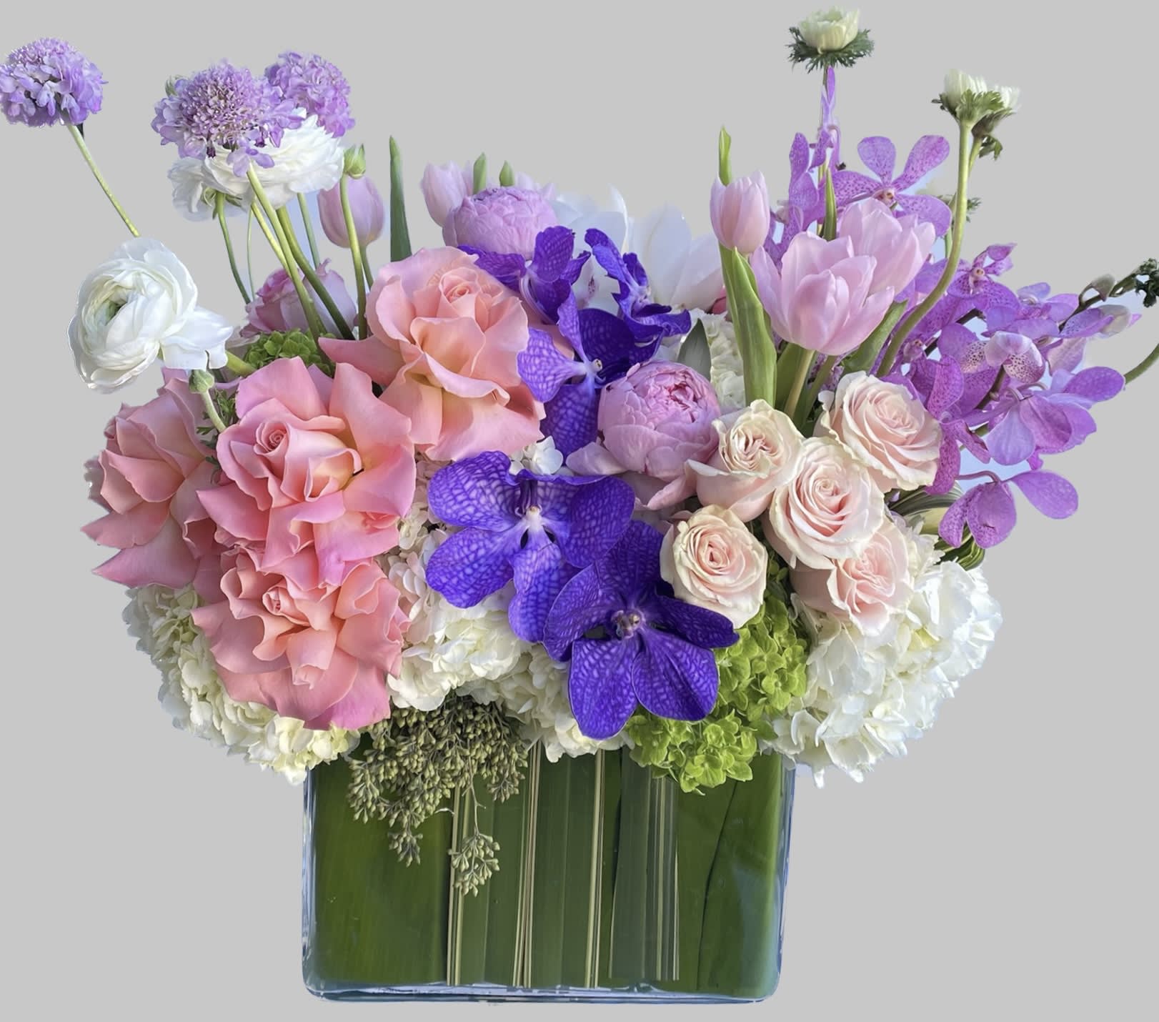 Pink roses and purple orchids arranged in a square glass vase