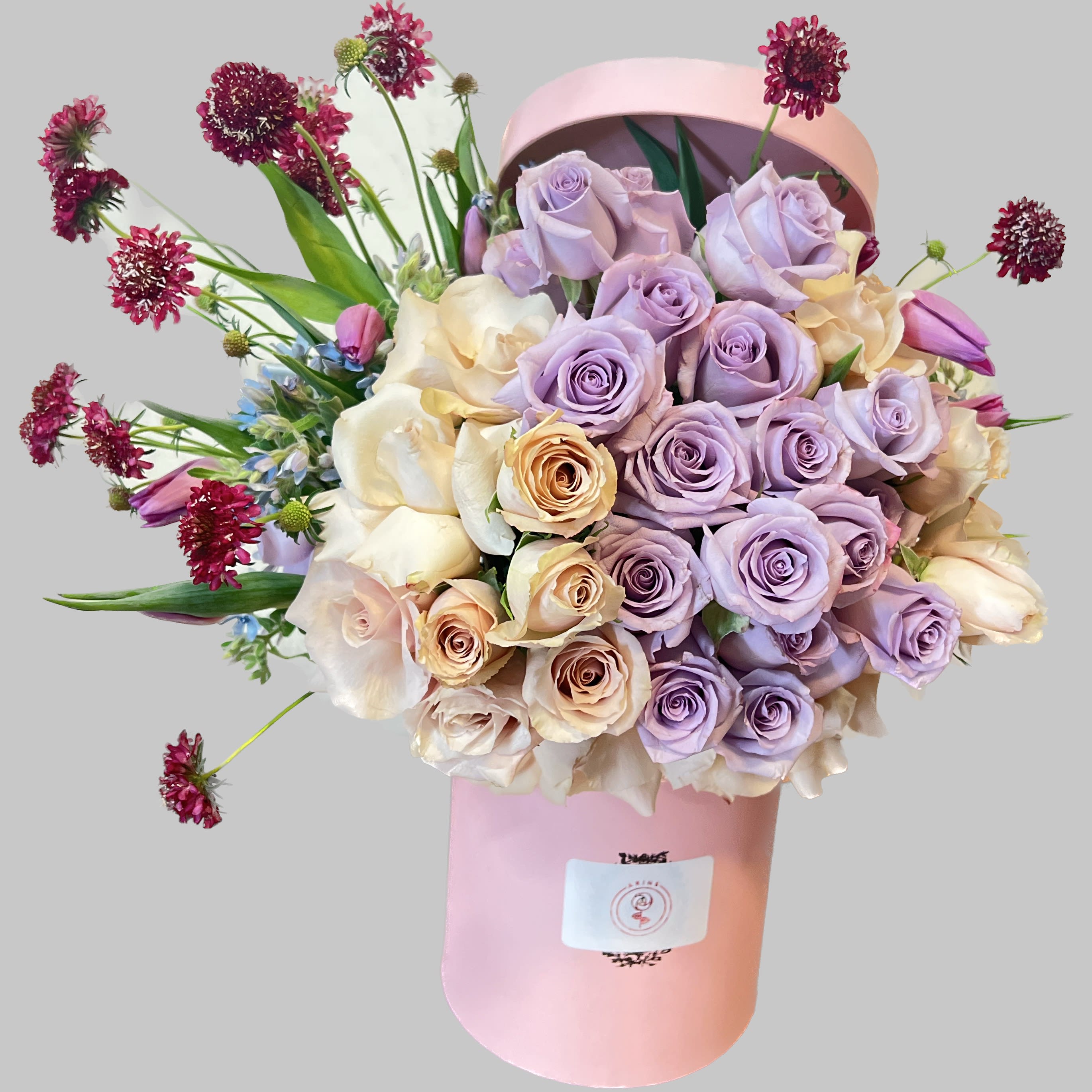 Lavender and cream rose bouquet in a pink hatbox with burgundy accent flowers