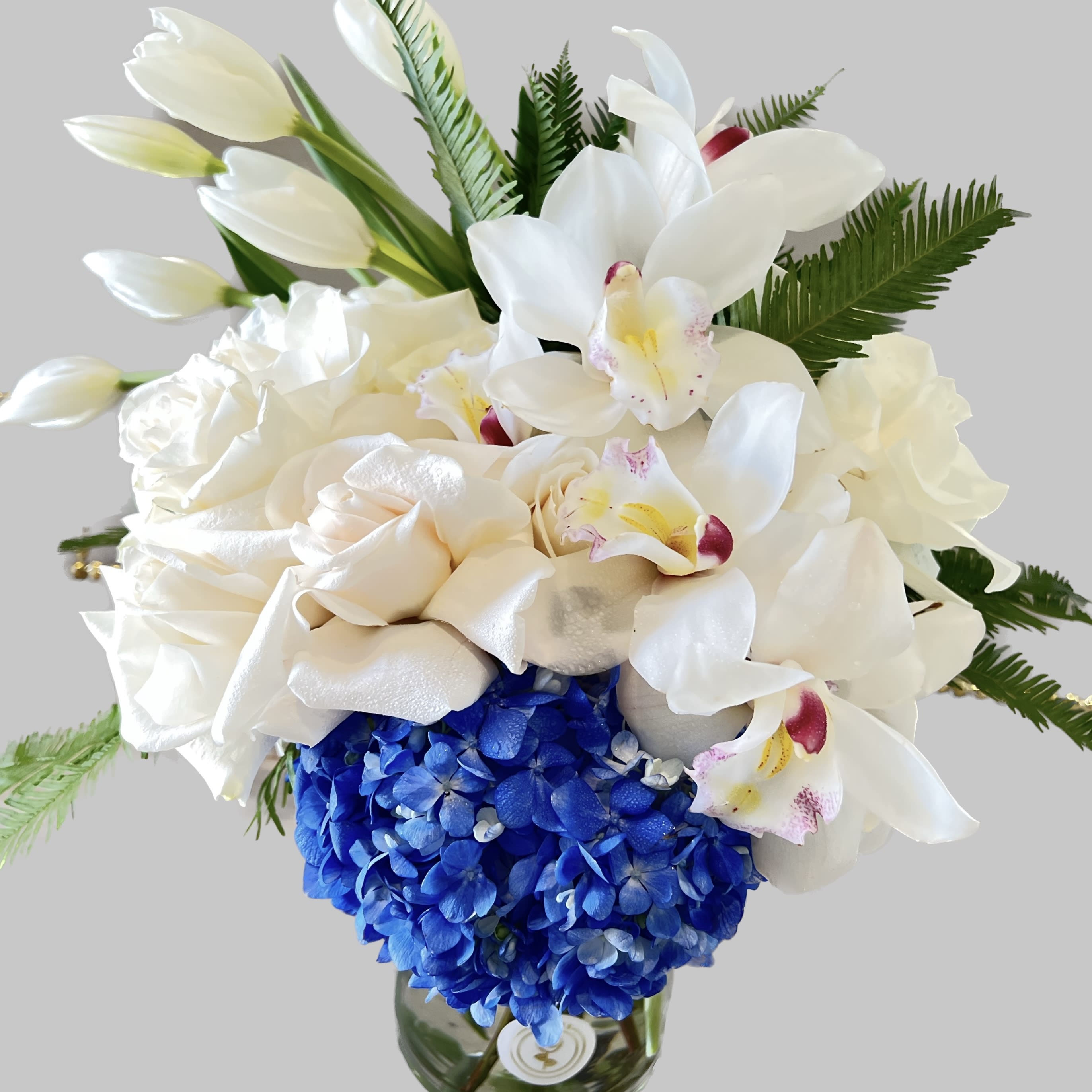Sterling - A blue and white arrangement in a clear glass vase, this arrangement is a cool colored dream. Featuring blue hydrangea, white cymbidium orchids, white tulips and white roses this arrangement makes a great gift  any occasion.  Approximate Dimensions: 10"D x 15”H