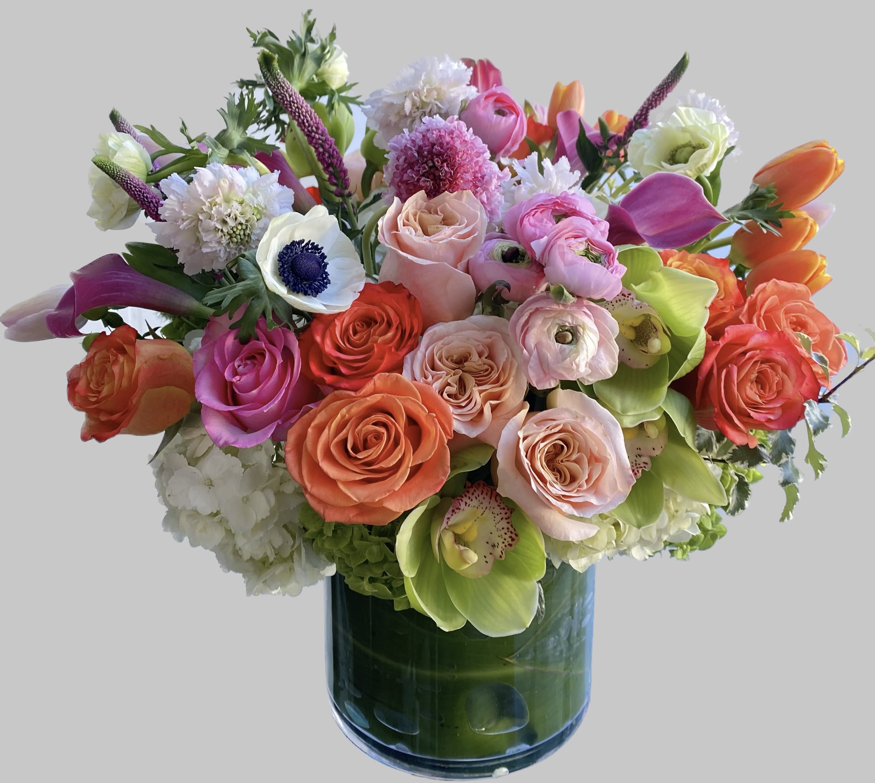 Mixed bouquet of roses, calla lilies, and orchids in a glass vase