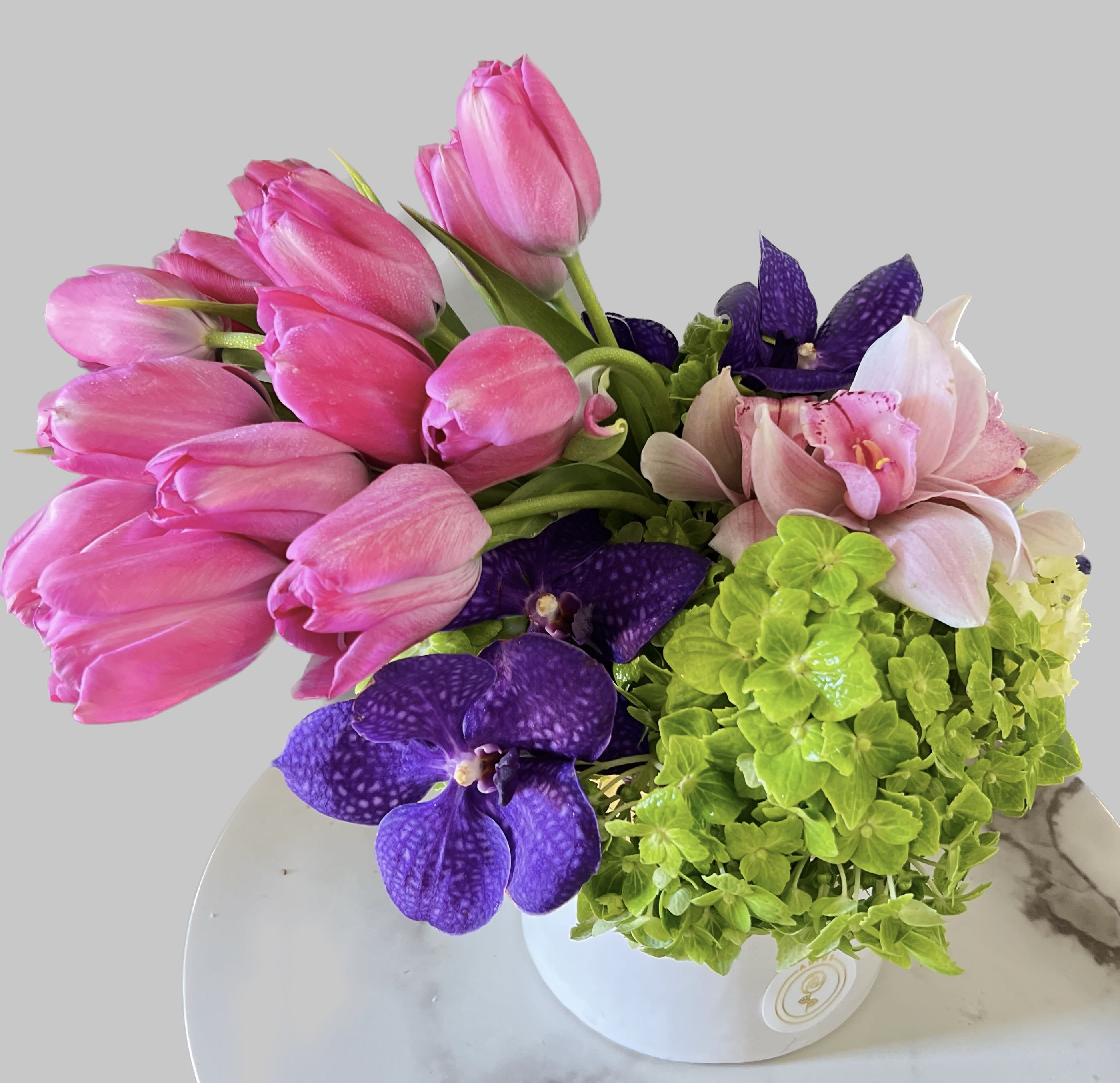 Pink tulips, purple orchids, and green hydrangeas in a white vase