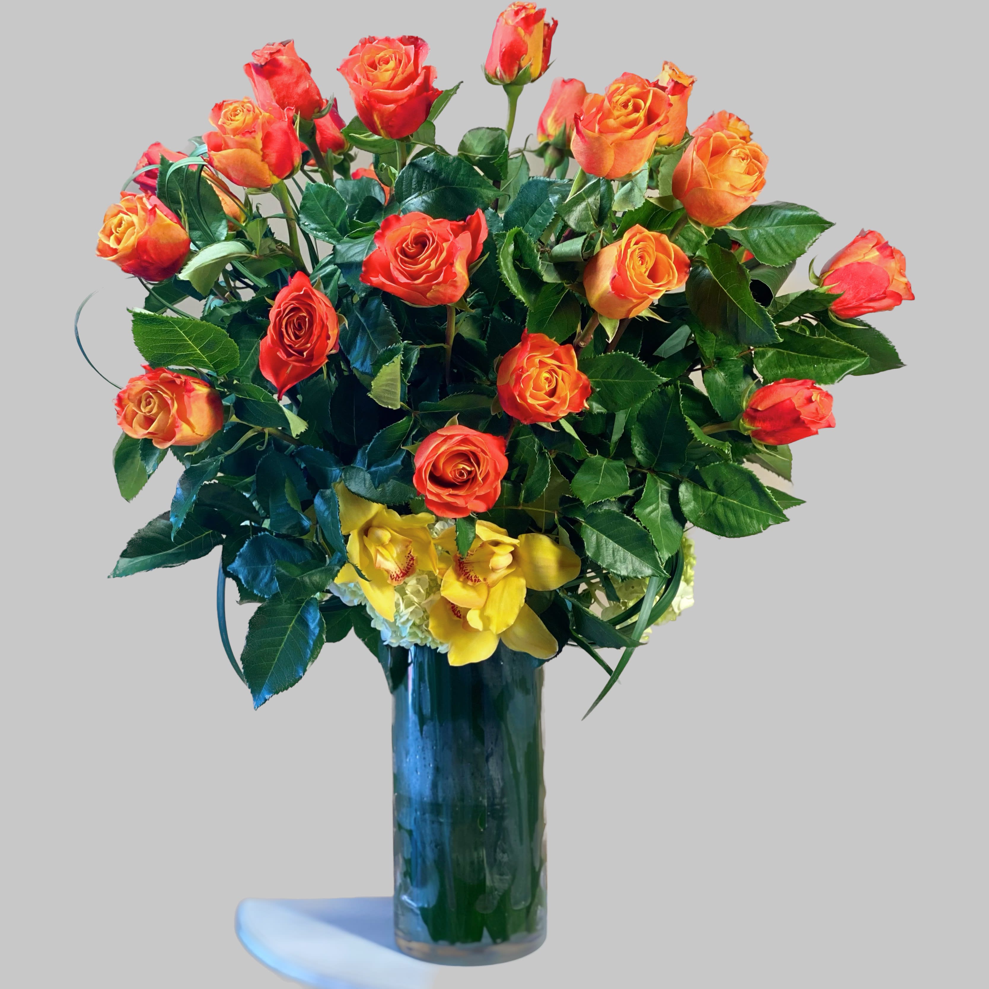 Bouquet of orange and red roses in a tall glass vase