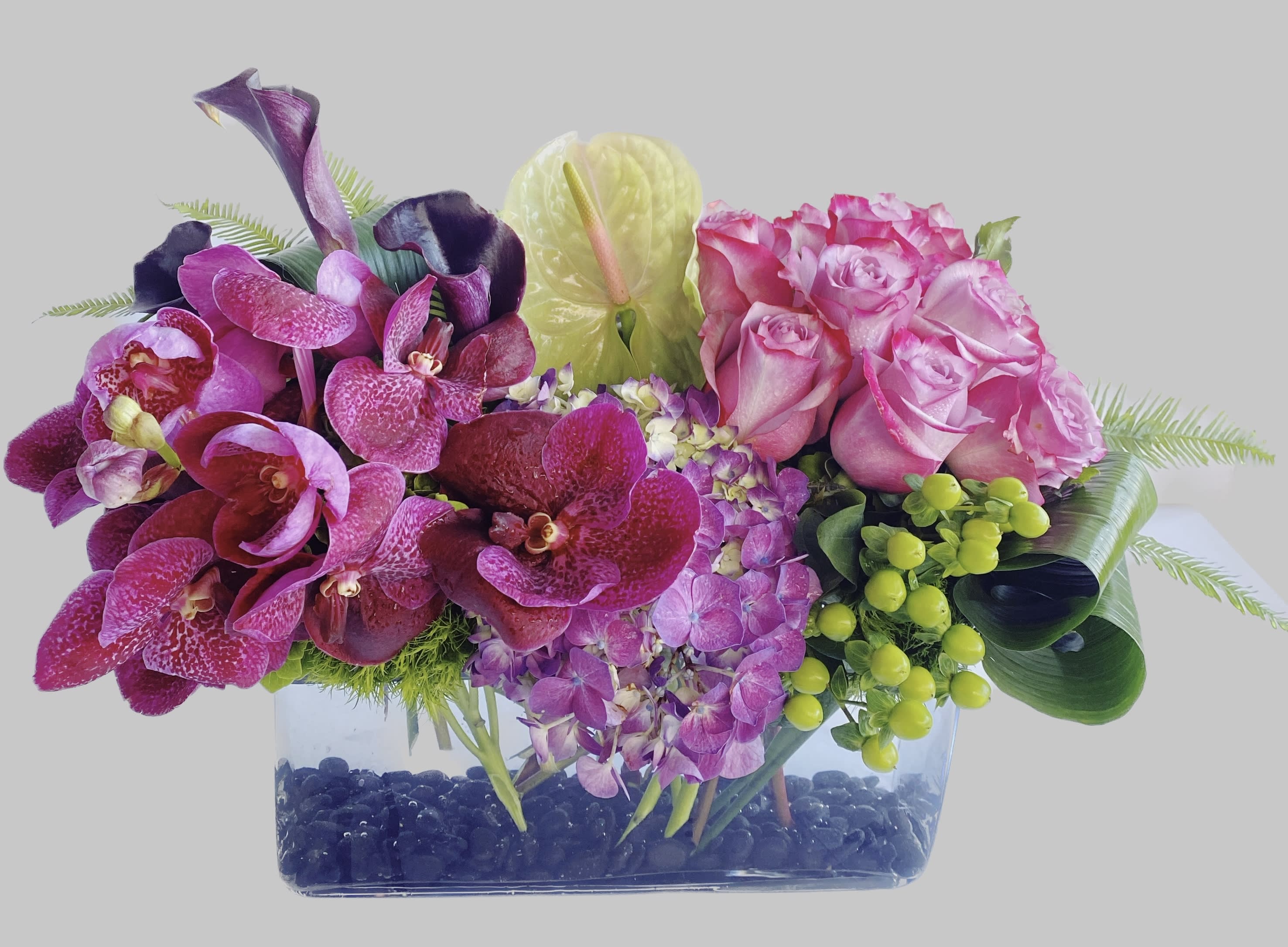 Pink roses and purple orchids in a clear rectangular vase