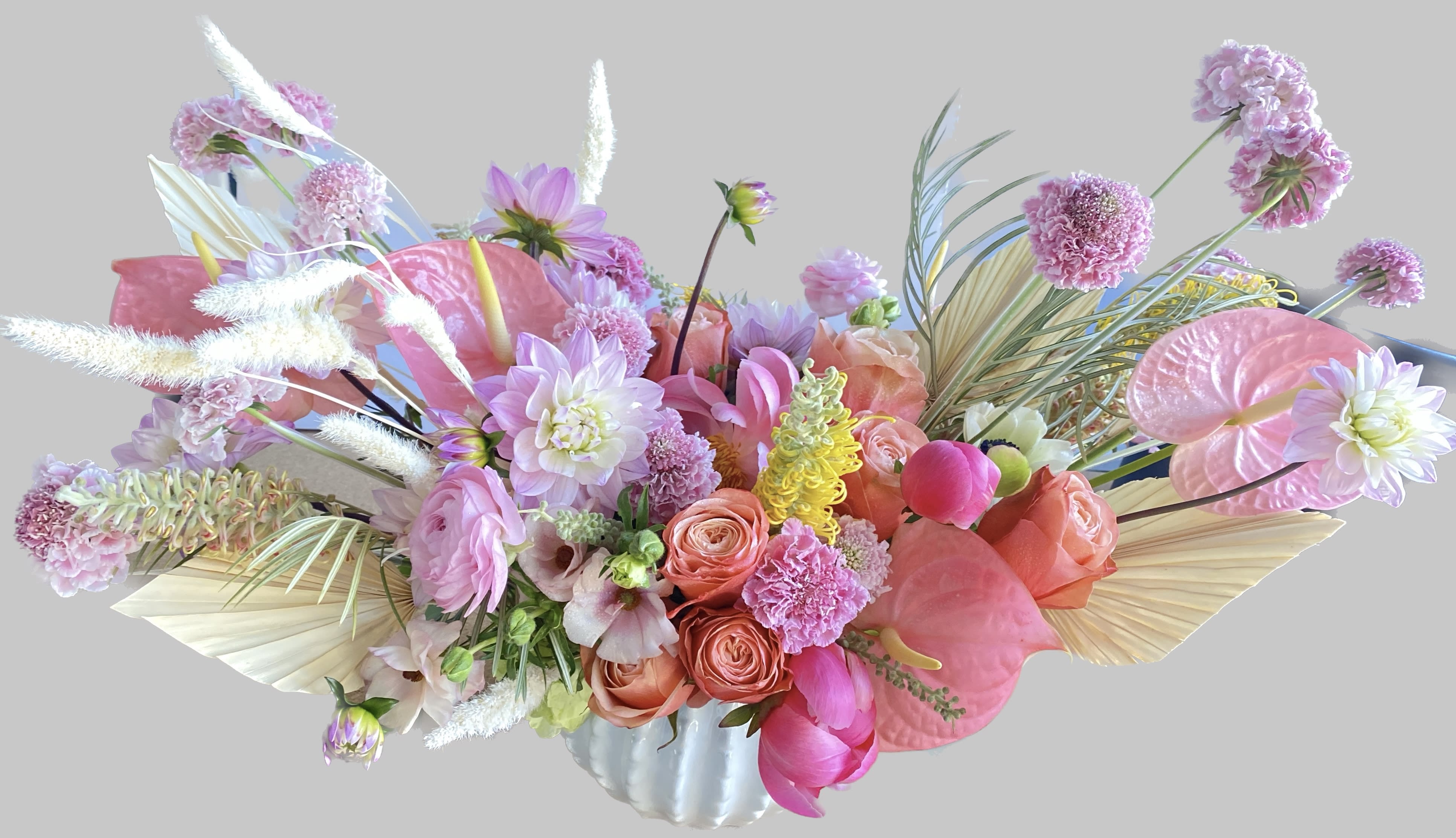 Pink and peach floral arrangement in a white vase with tropical leaves