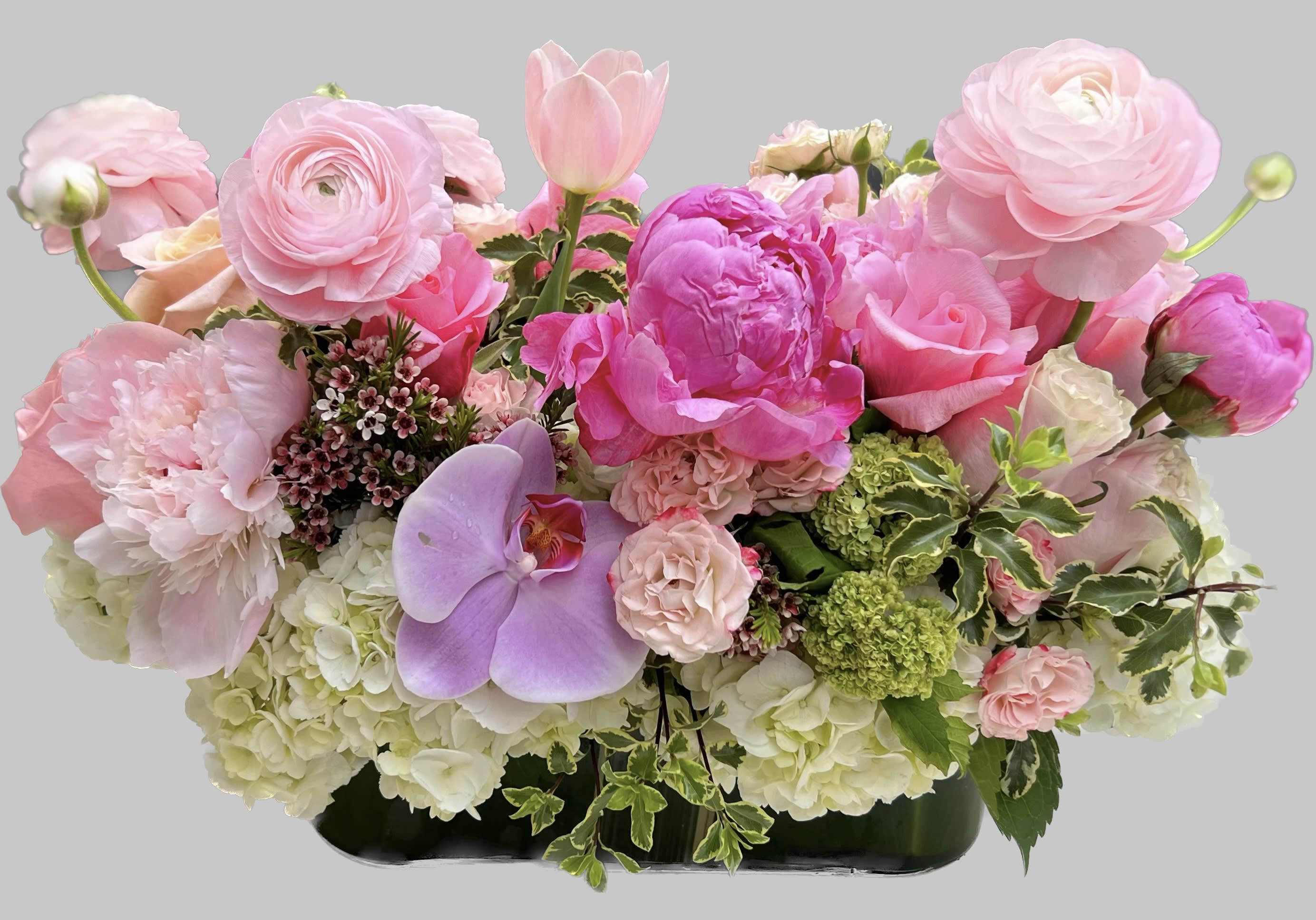 Pink floral arrangement with peonies, roses, tulips, and orchids in a low container