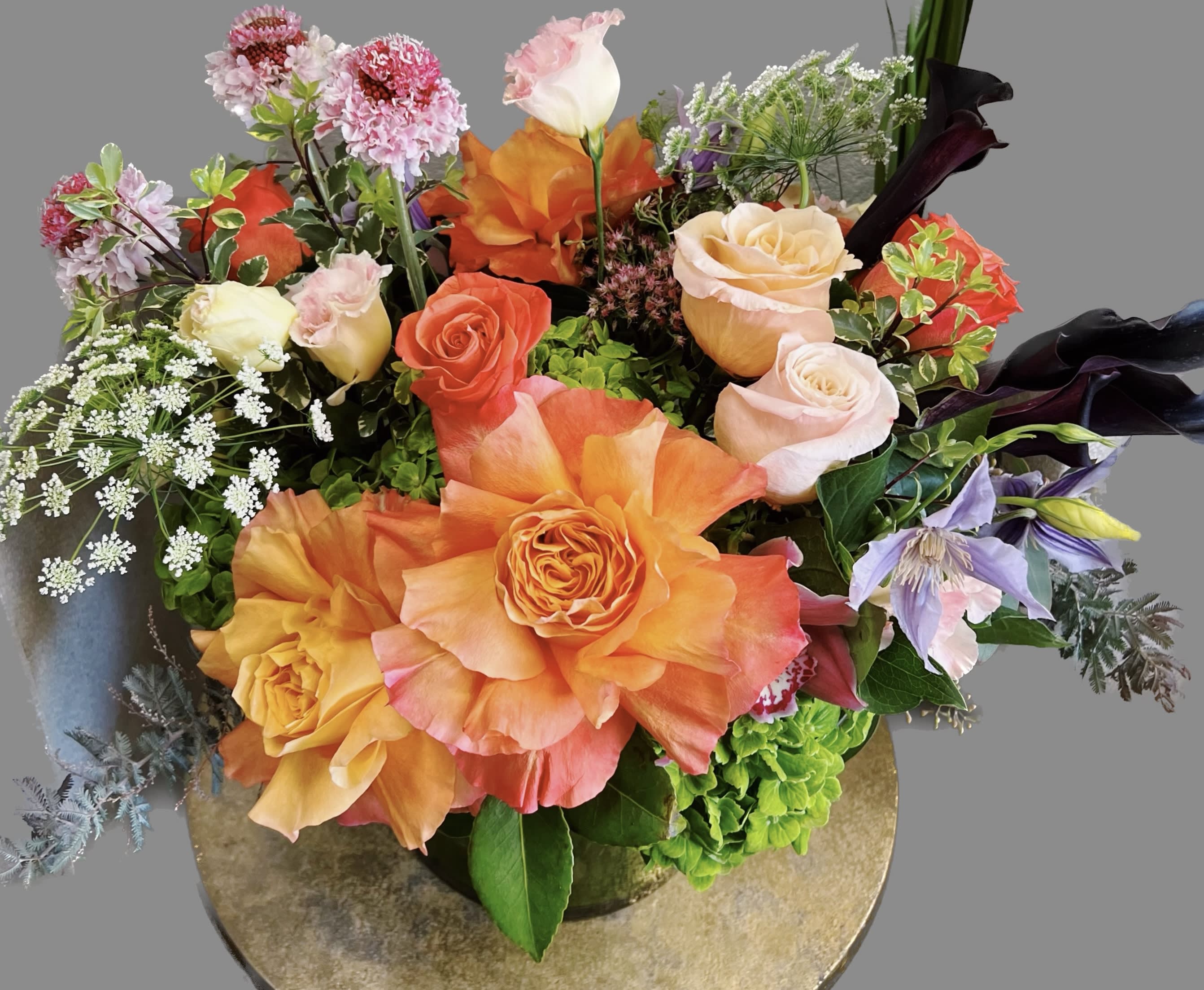 Mixed bouquet of orange, pink, and cream roses with purple blooms in a vase