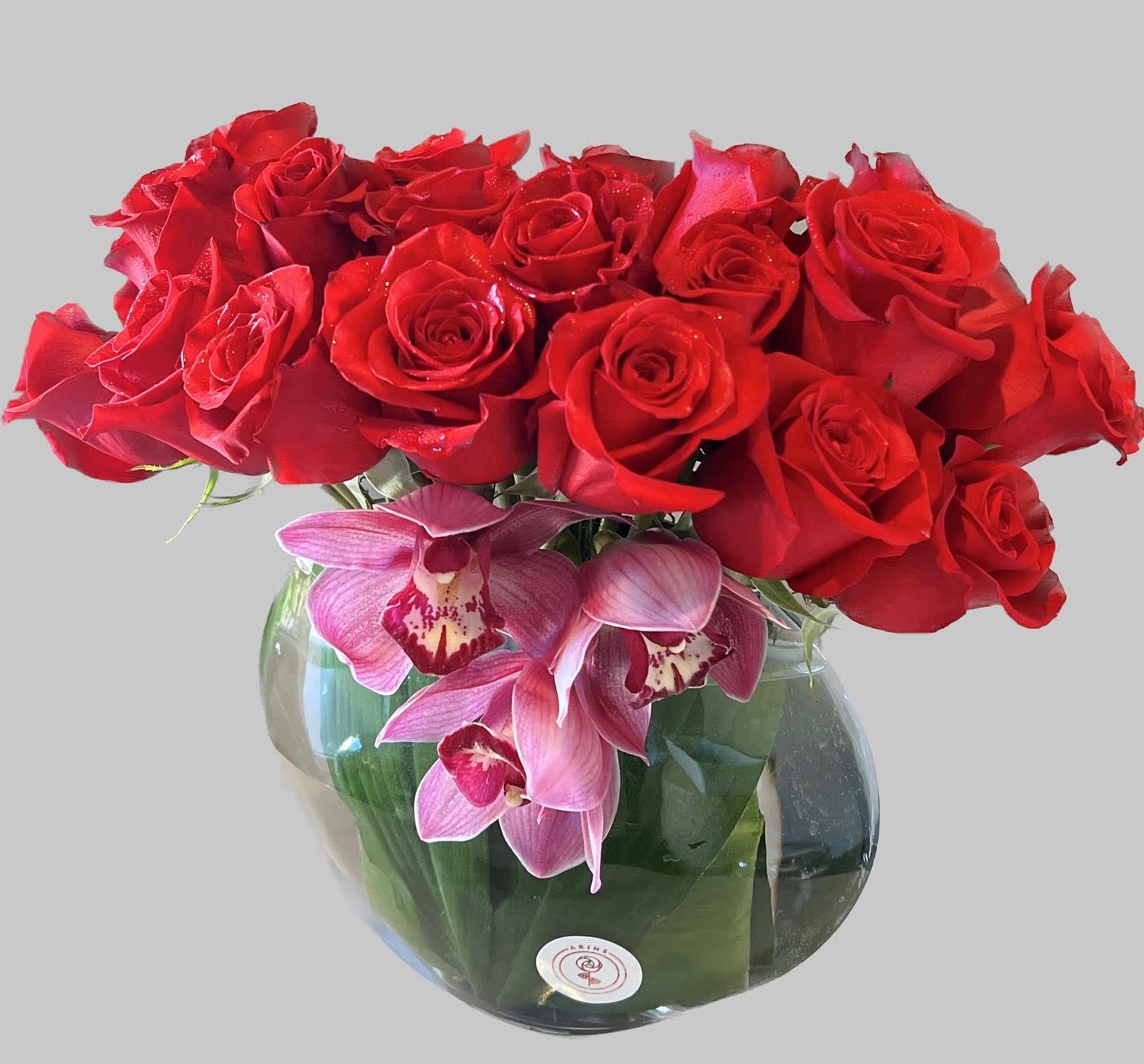 Red roses and pink orchids arranged in a round glass vase.