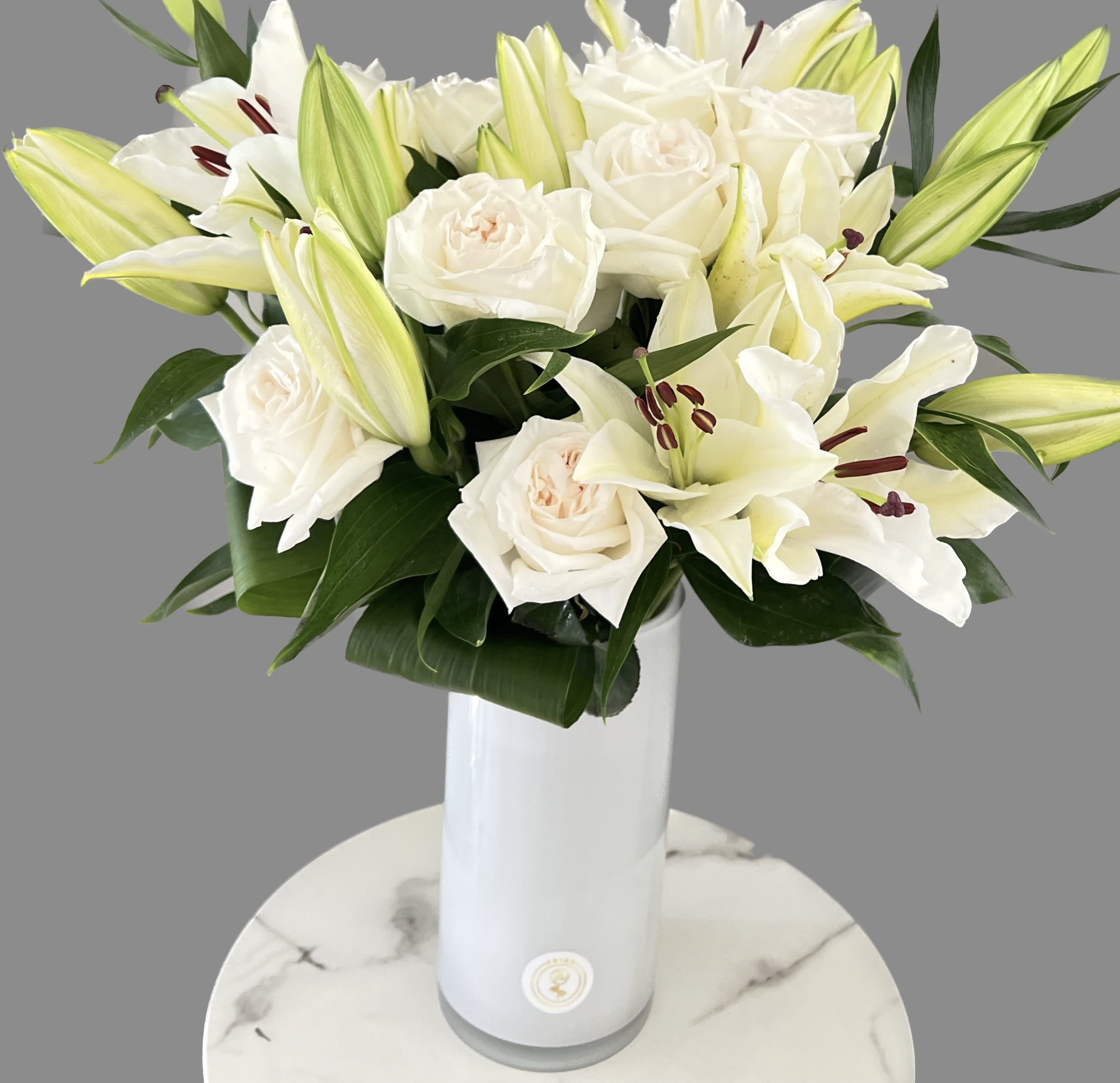 White roses and lilies arranged in a tall white vase.