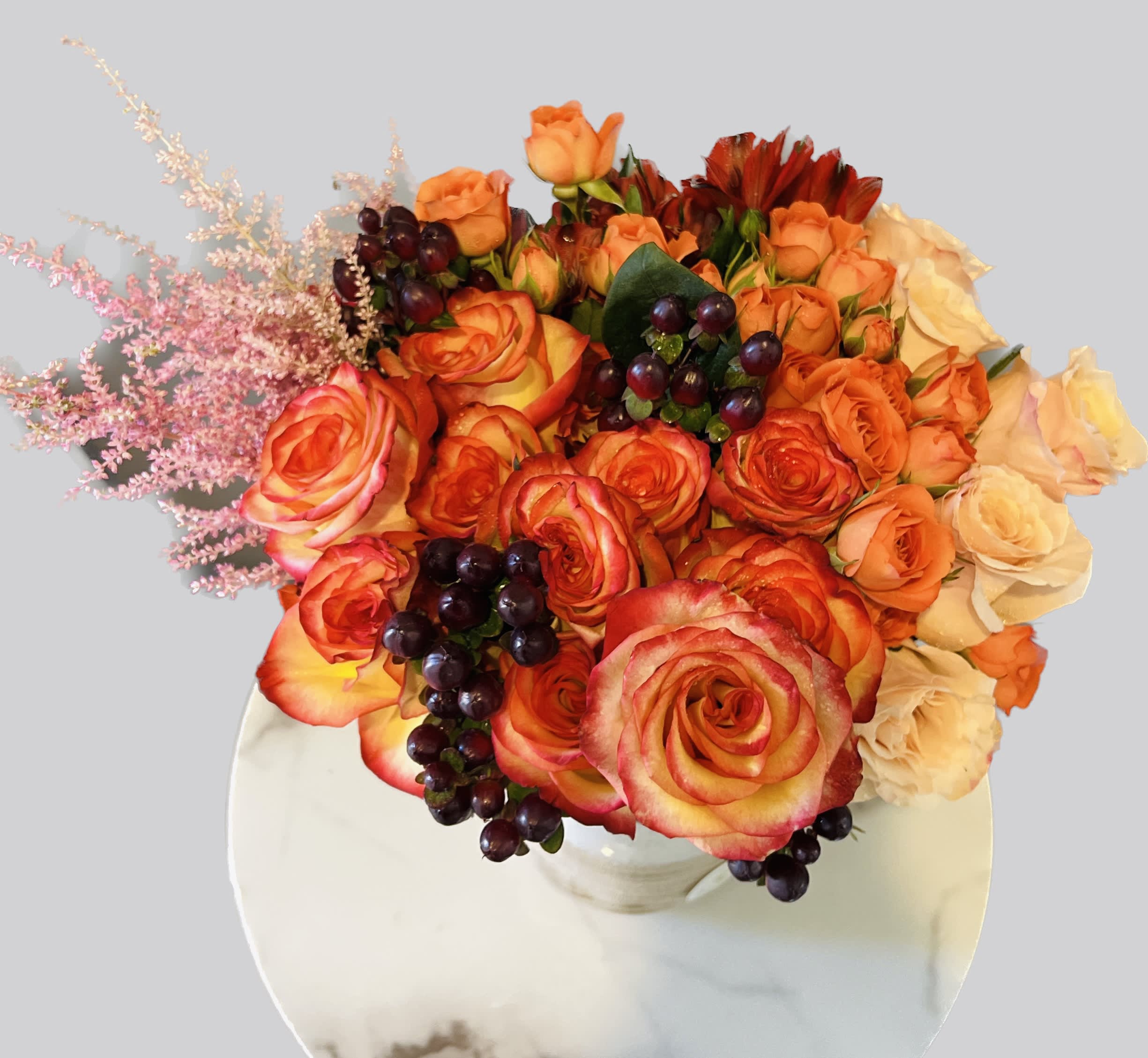 Bouquet of orange and cream roses with dark berries in a white vase