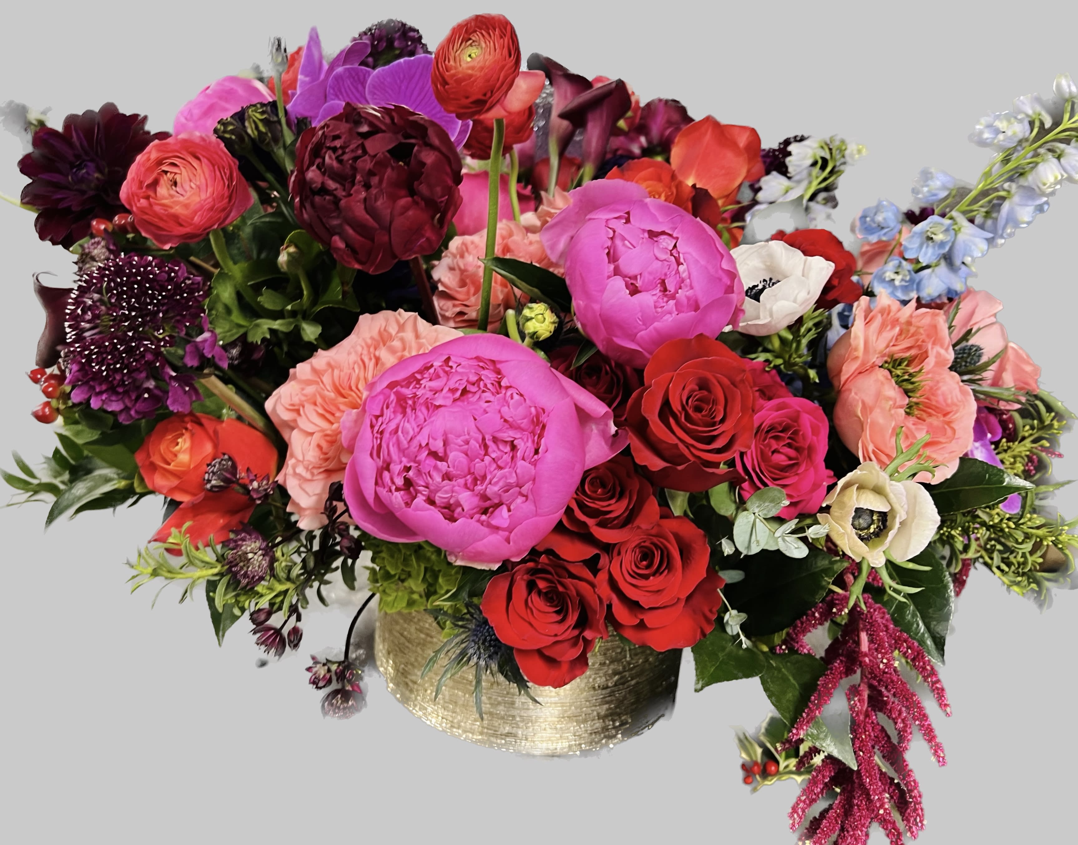 Mixed bouquet of bright pink, red, and purple flowers in a gold vase
