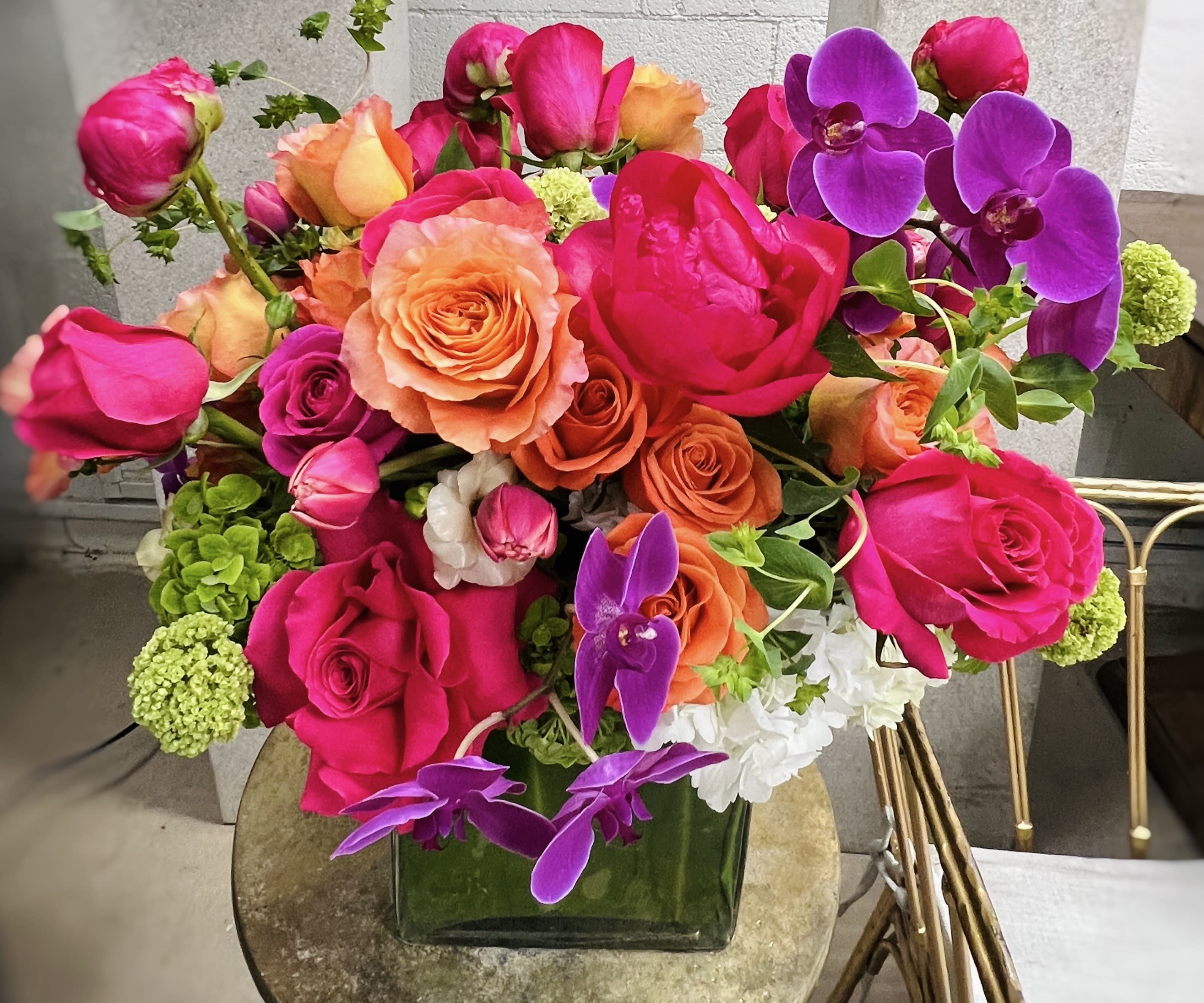 Bright bouquet of pink, orange, and purple roses in a square glass vase