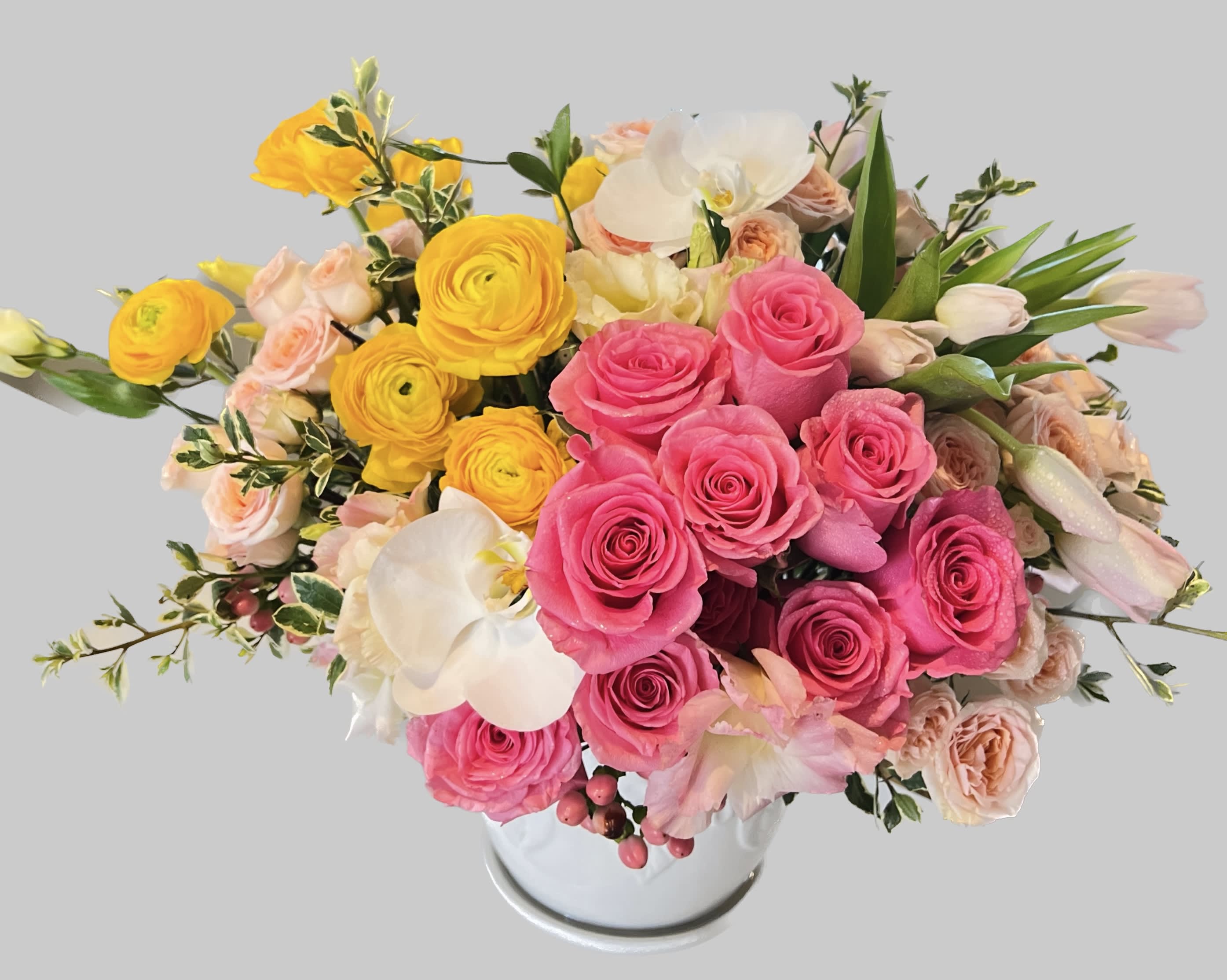 Pink and yellow roses arranged in a white vase with white orchids