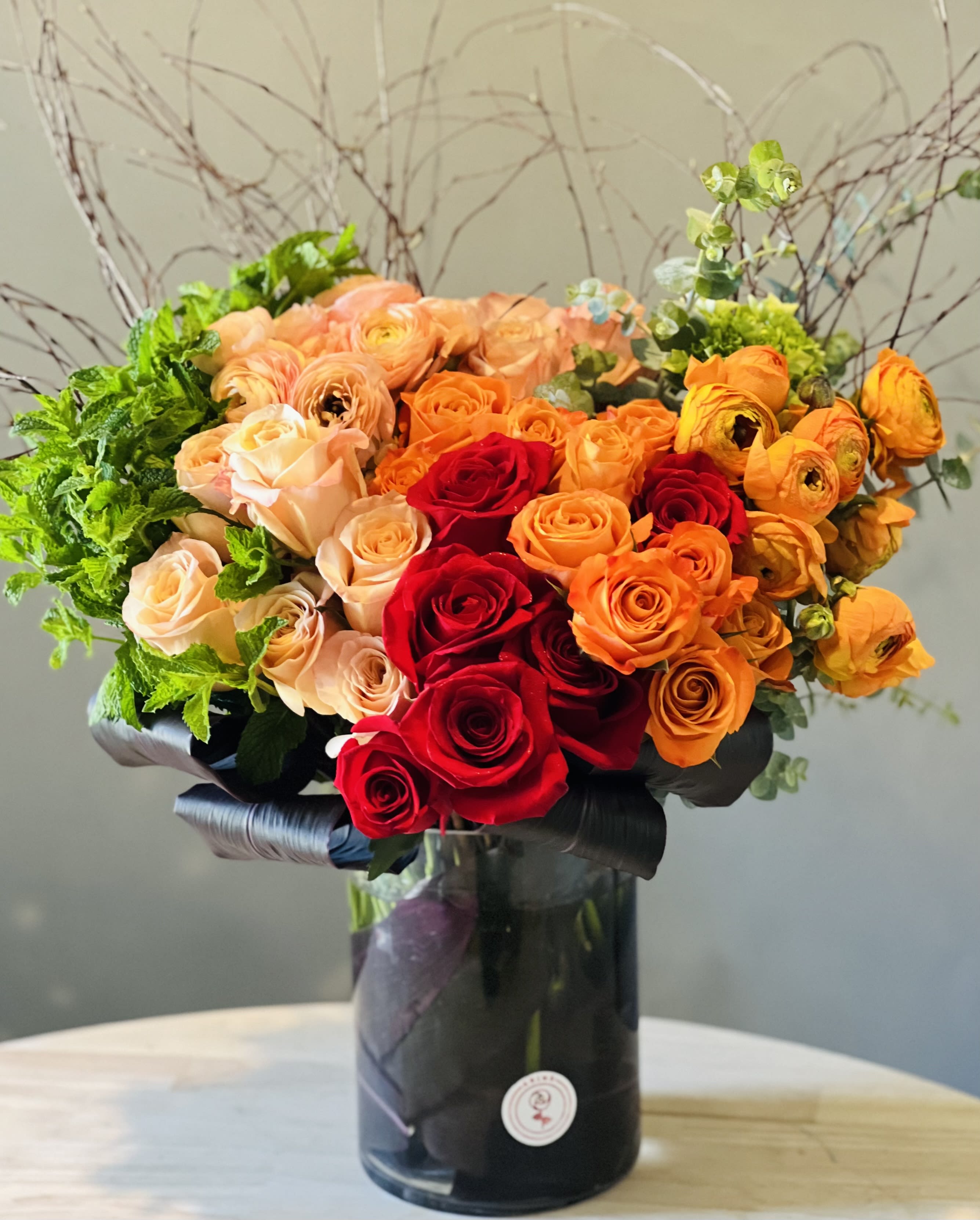 Bouquet of red, orange, and peach roses in a black vase
